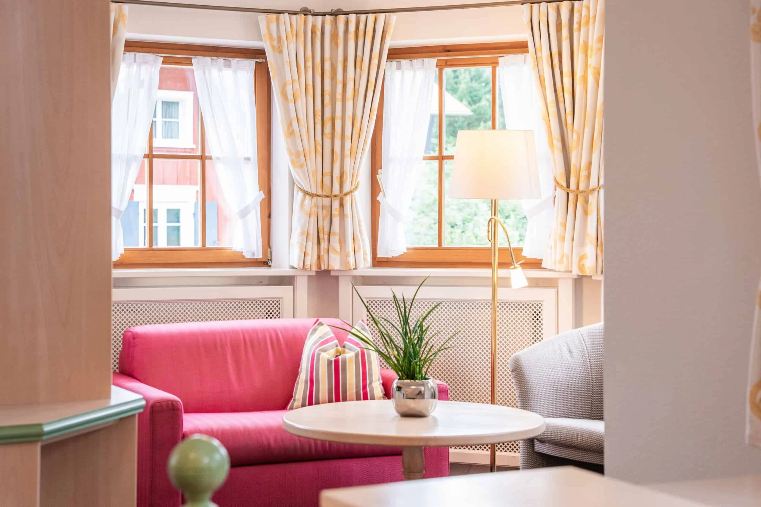 Sitzecke mit pinkfarbenem Sofa, rundem Tisch und Erkerfenstern