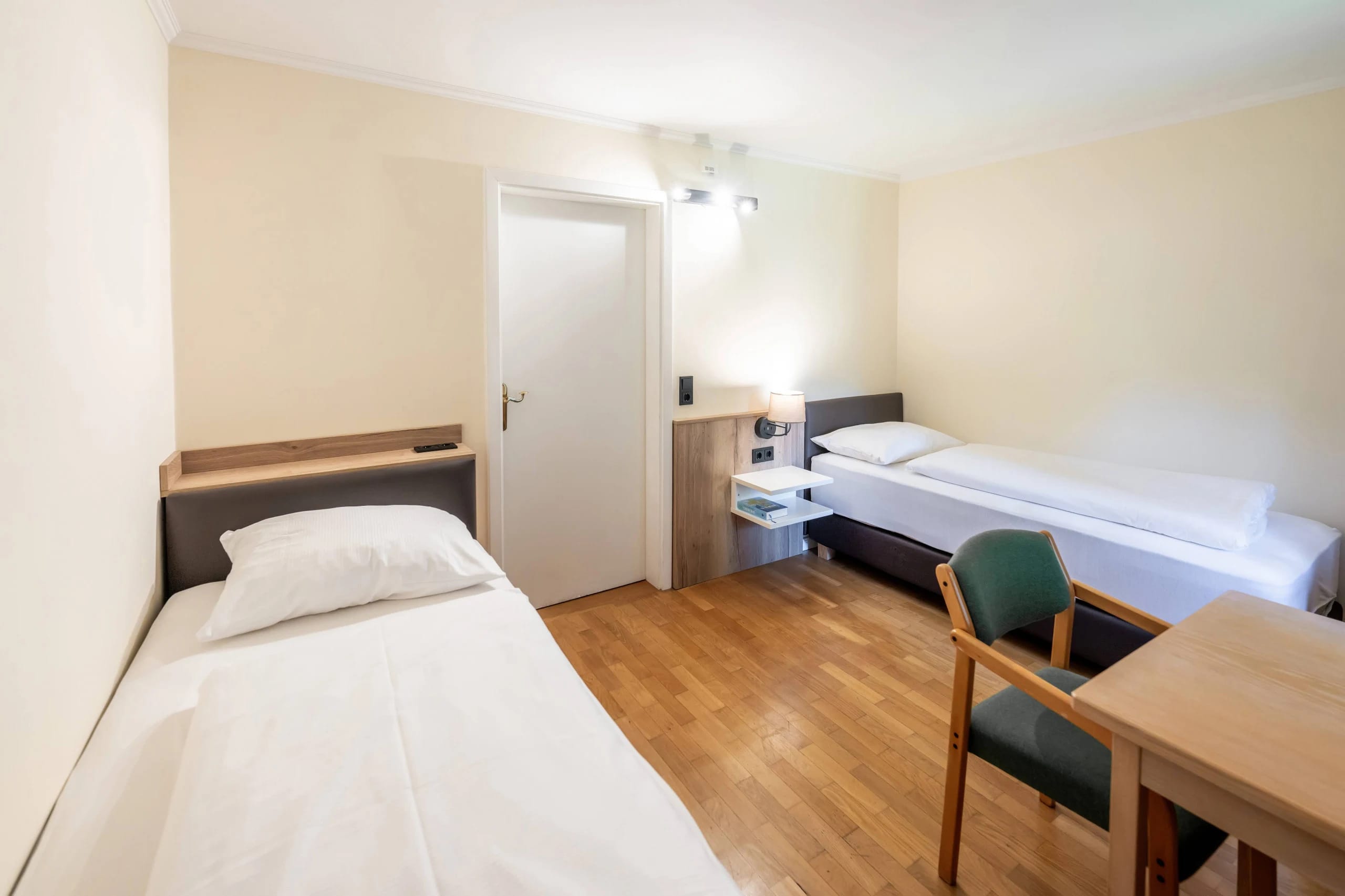 Zweibettzimmer mit zwei Einzelbetten, kleinem Schreibtisch und Holzboden