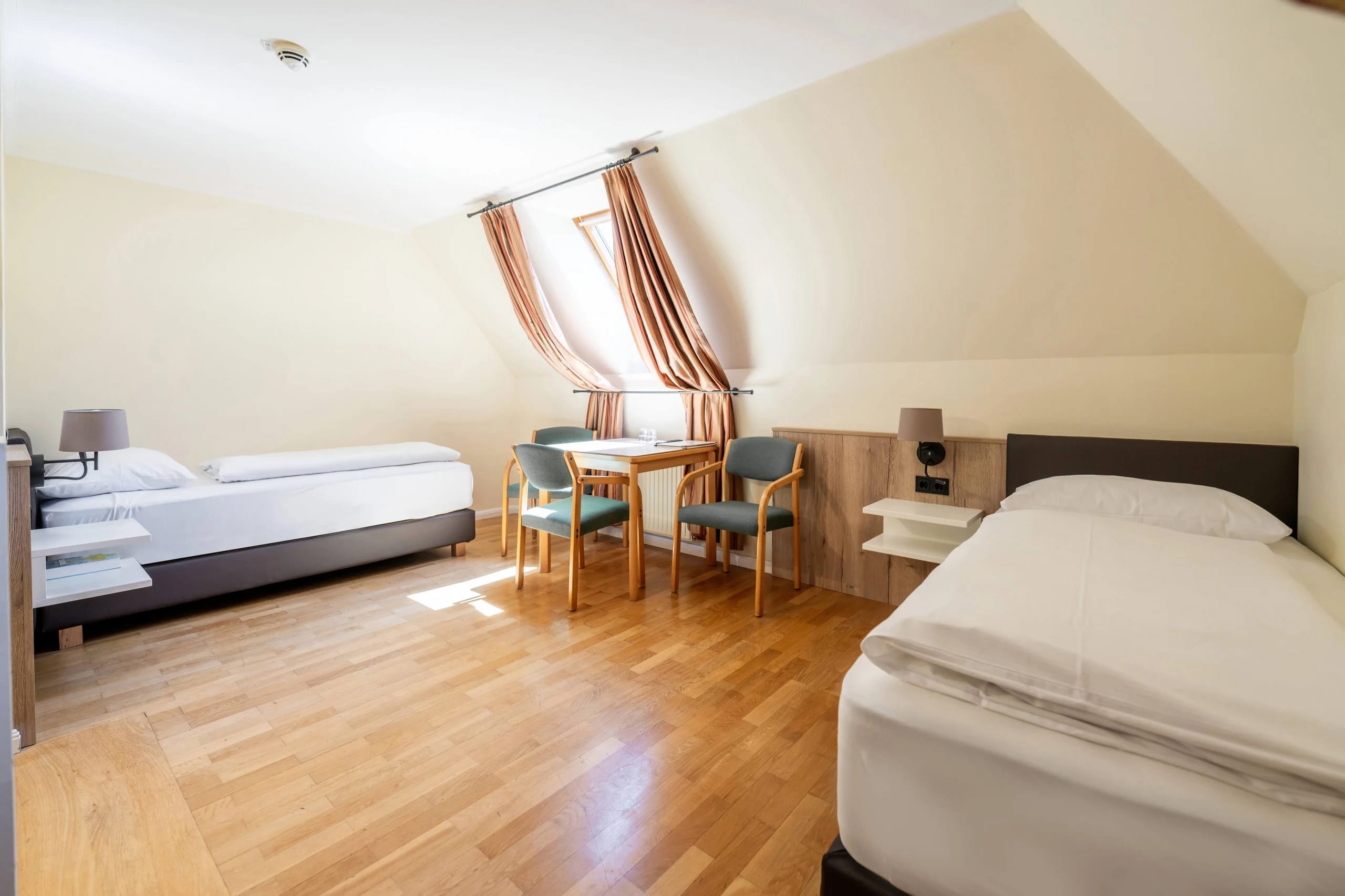 Dreibettzimmer im Dachgeschoss mit Dachfenster, Tisch mit zwei Stühlen und drei Betten
