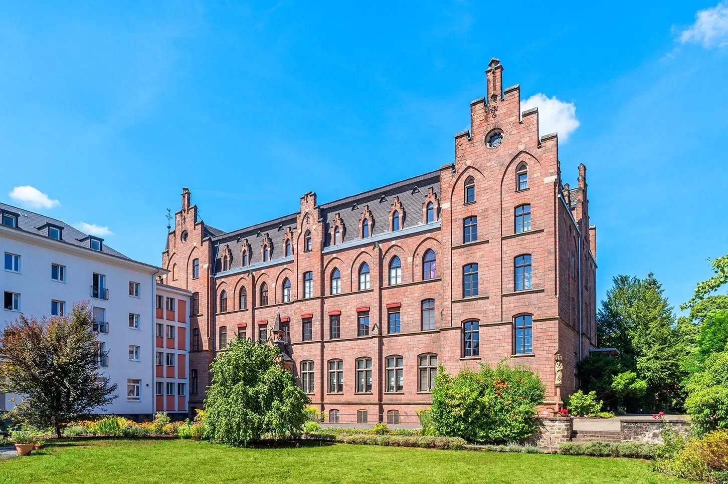 Backsteingebäude mit spitzen Türmchen und Vorgarten unter blauem Himmel