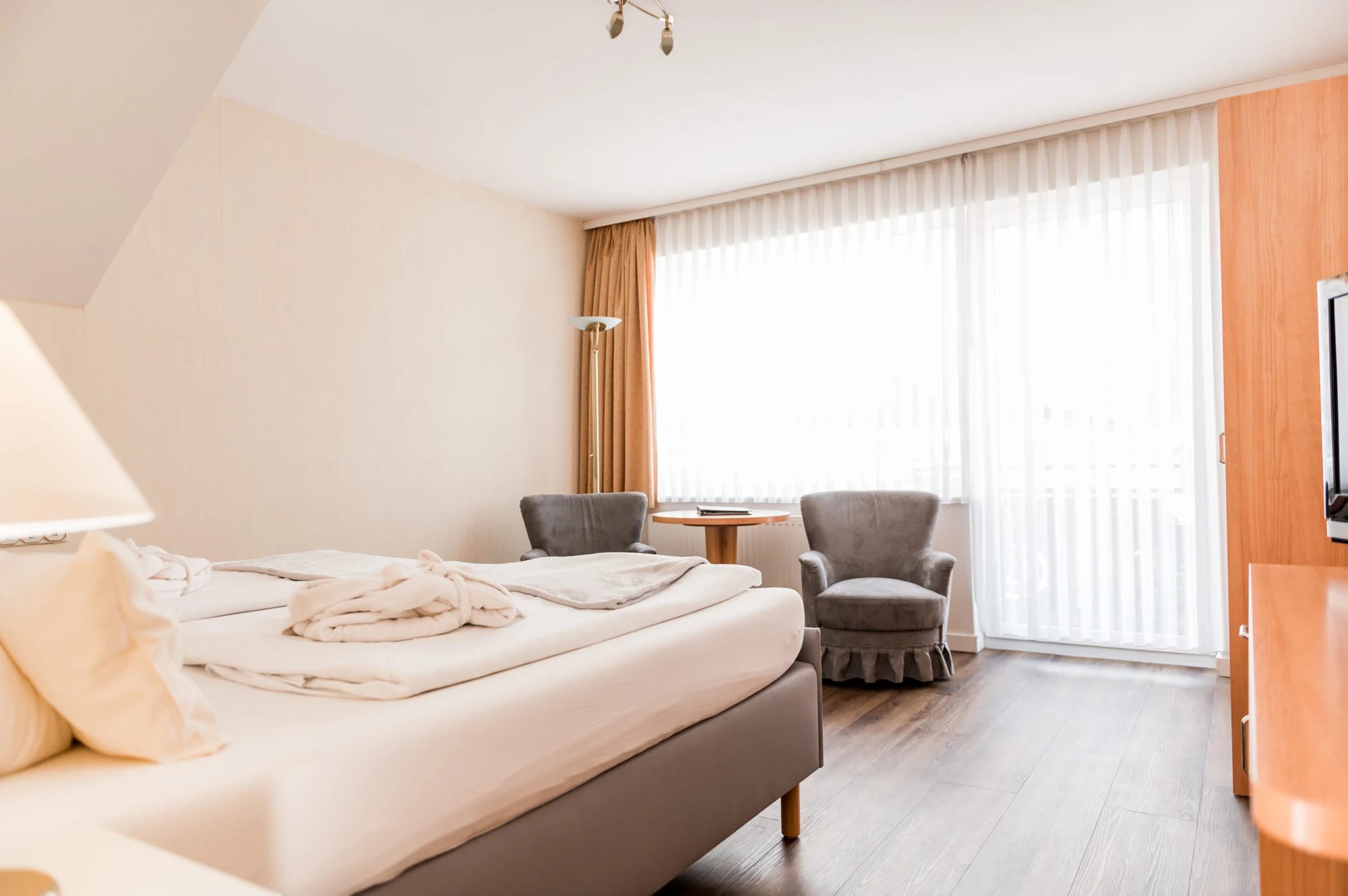 Doppelzimmer mit zwei Sesseln, kleinem Tisch und bodentiefem Fenster