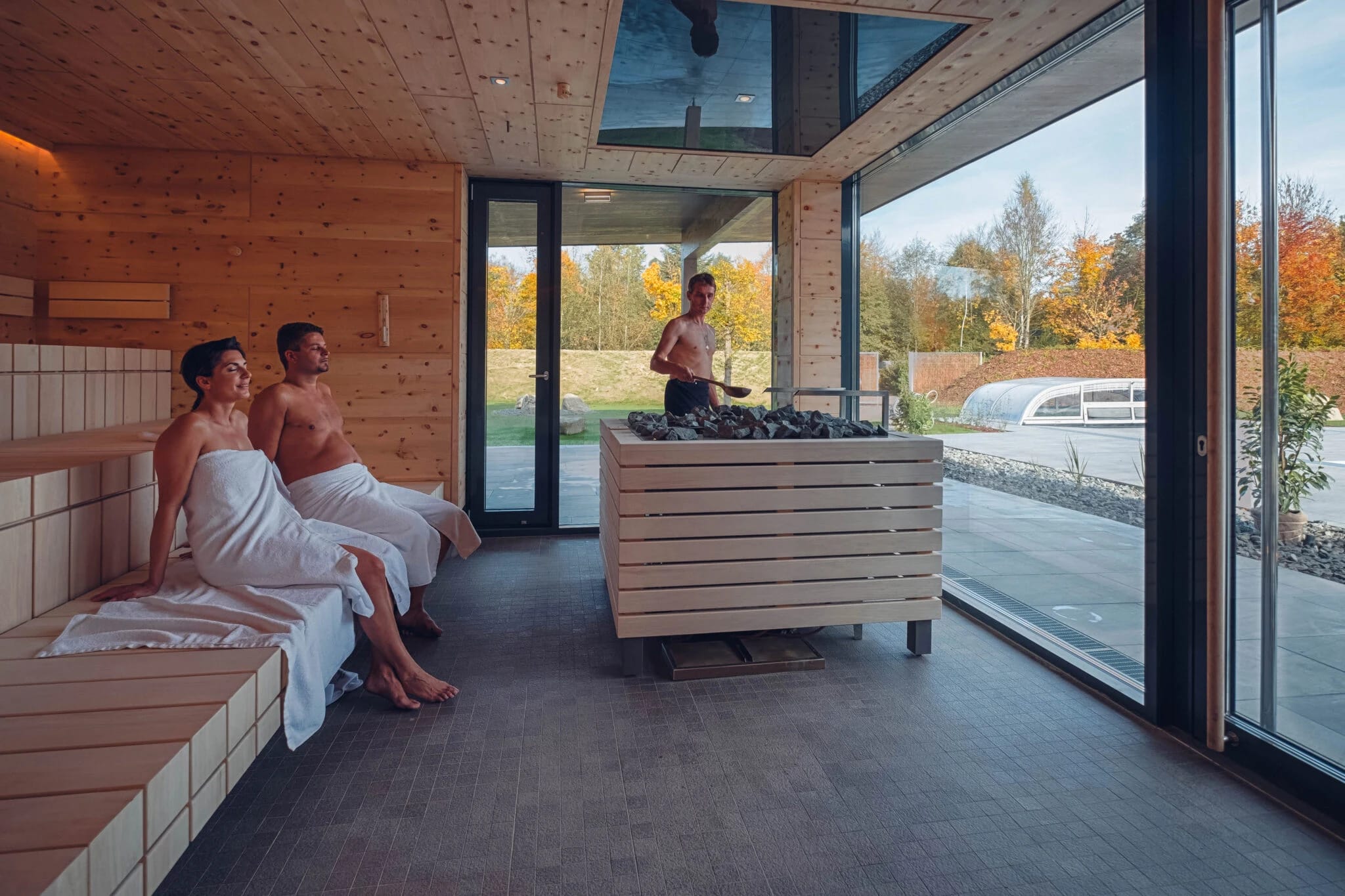 Moderne Saunakabine aus Holz mit Saunaofen und bodentiefen Fenstern ins Grüne