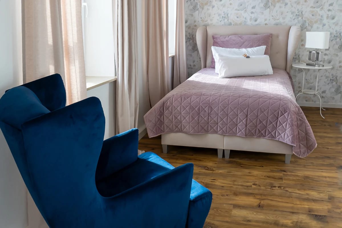 Einzelzimmer mit blauem Ohrensessel und altrosa Tagesdecke