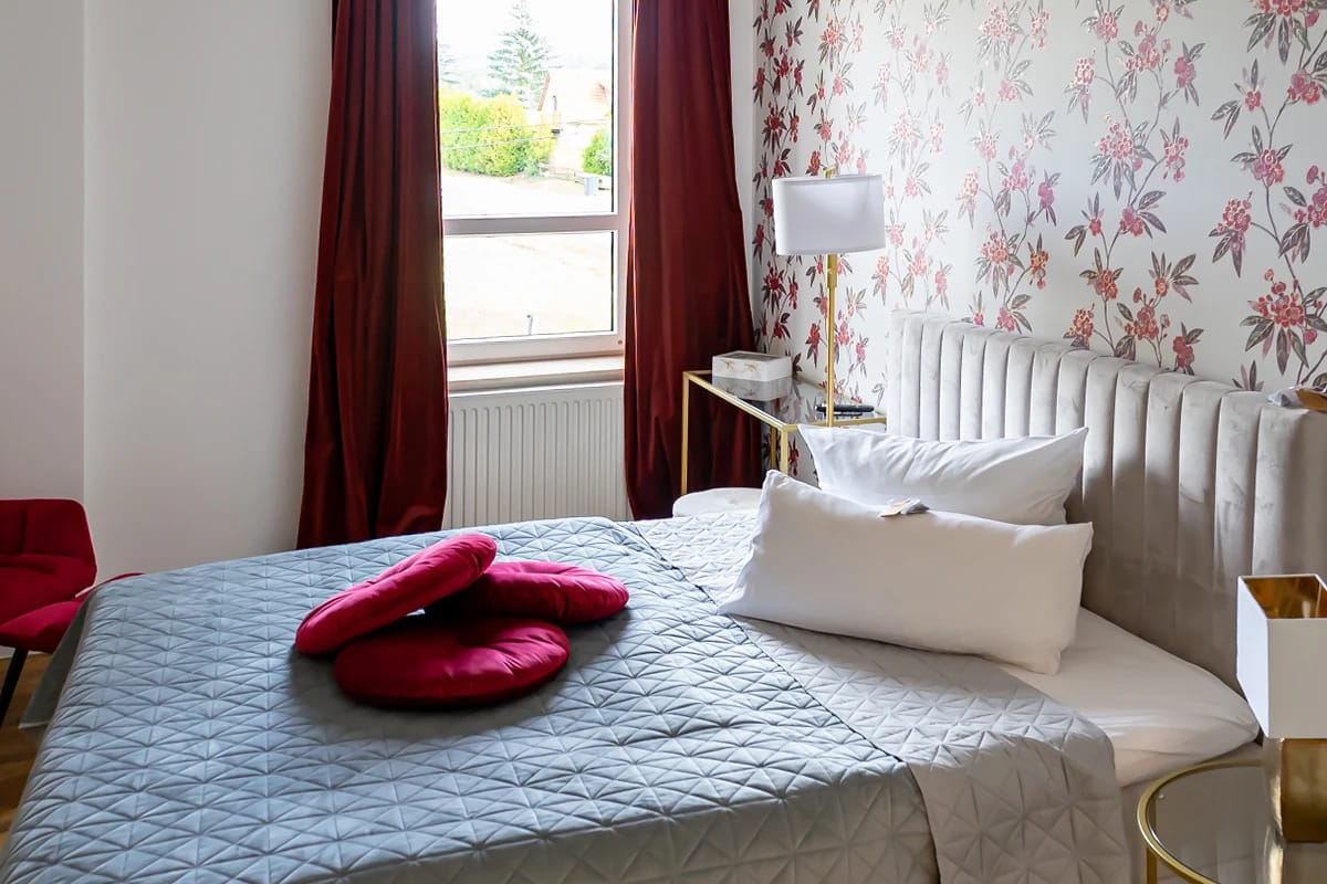 Zimmer mit floraler Tapete, roten Vorhängen und Fensterblick