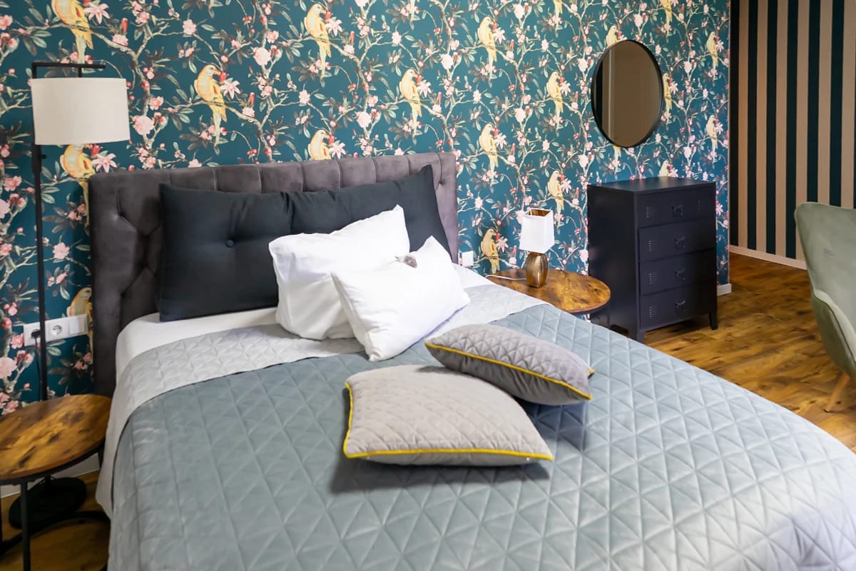 Doppelzimmer mit dunkelgrüner Blumentapete und grauem Bett
