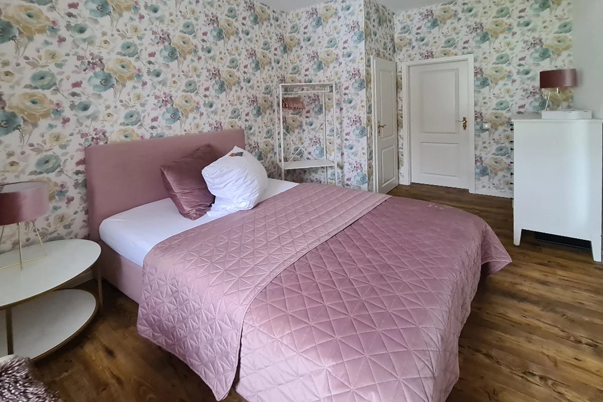 Einzelzimmer mit heller Blumentapete und altrosa Tagesdecke