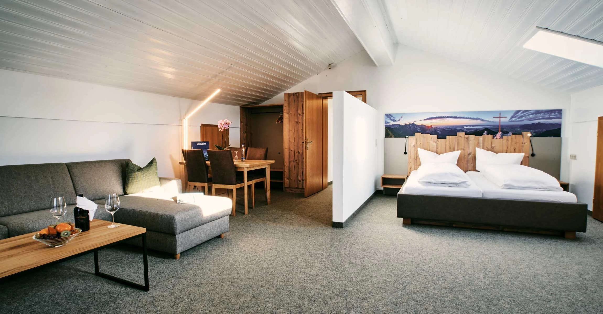 Geräumiges Doppelzimmer mit Sofaecke, Esstisch und Bett vor einem großen Bergmotiv an der Wand