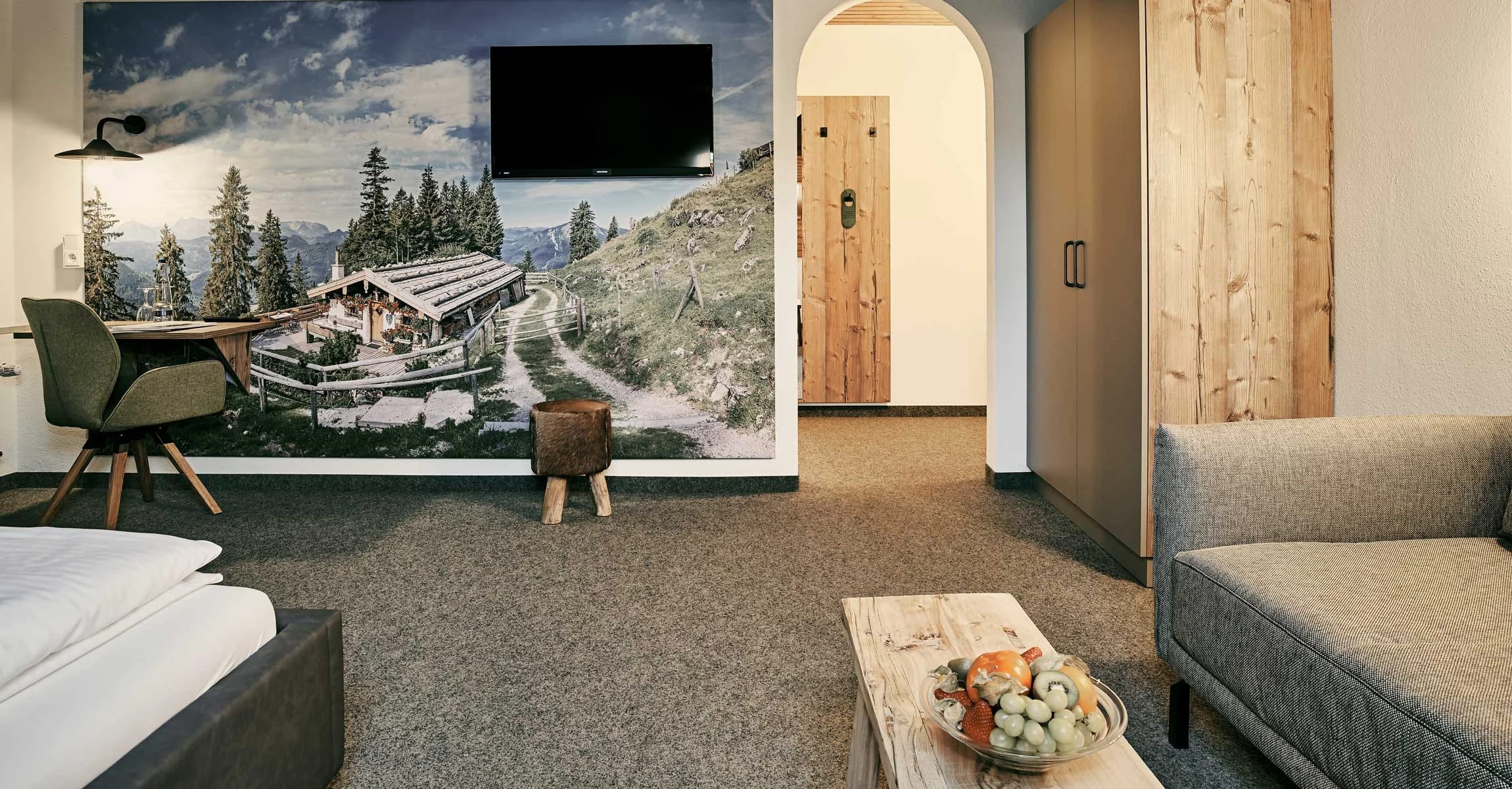 Modernes Zimmer mit Wandbild einer Almhütte, Sessel, Sofa und heller Holztür
