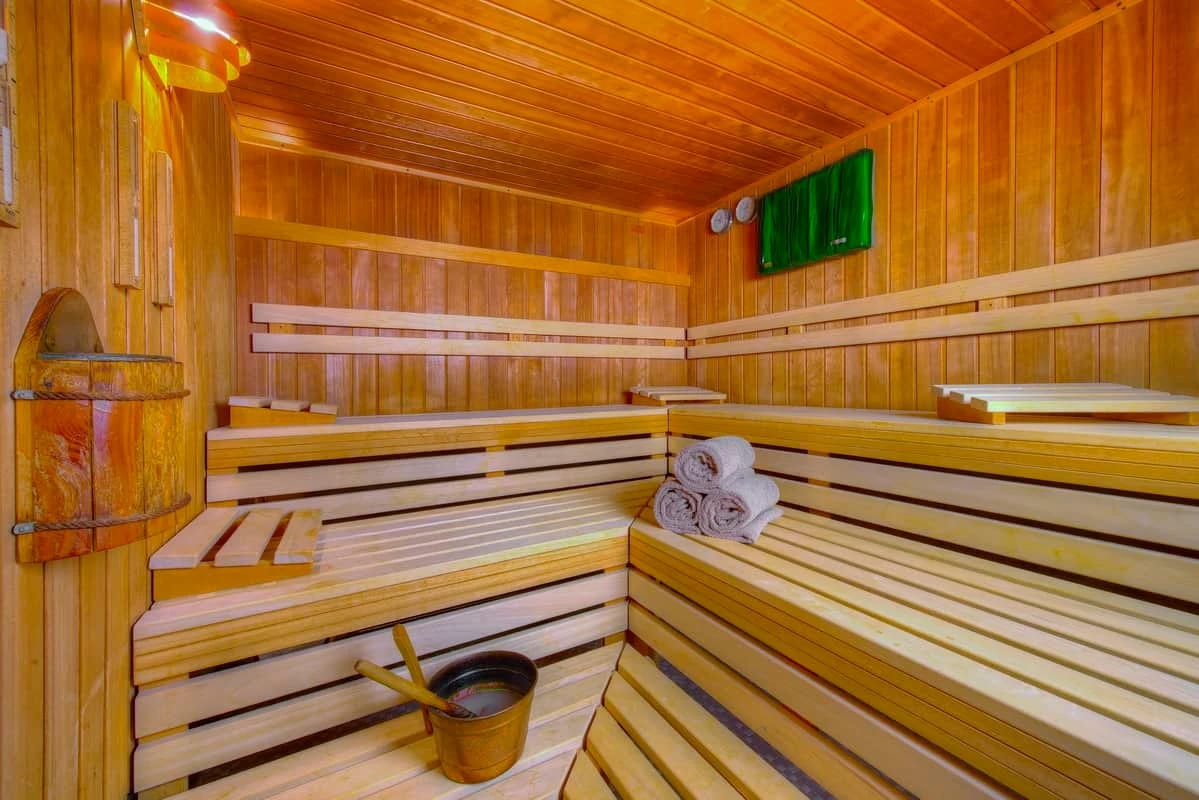 Sauna mit hellen Holzbänken, Aufgusskübel und gerollten Handtüchern