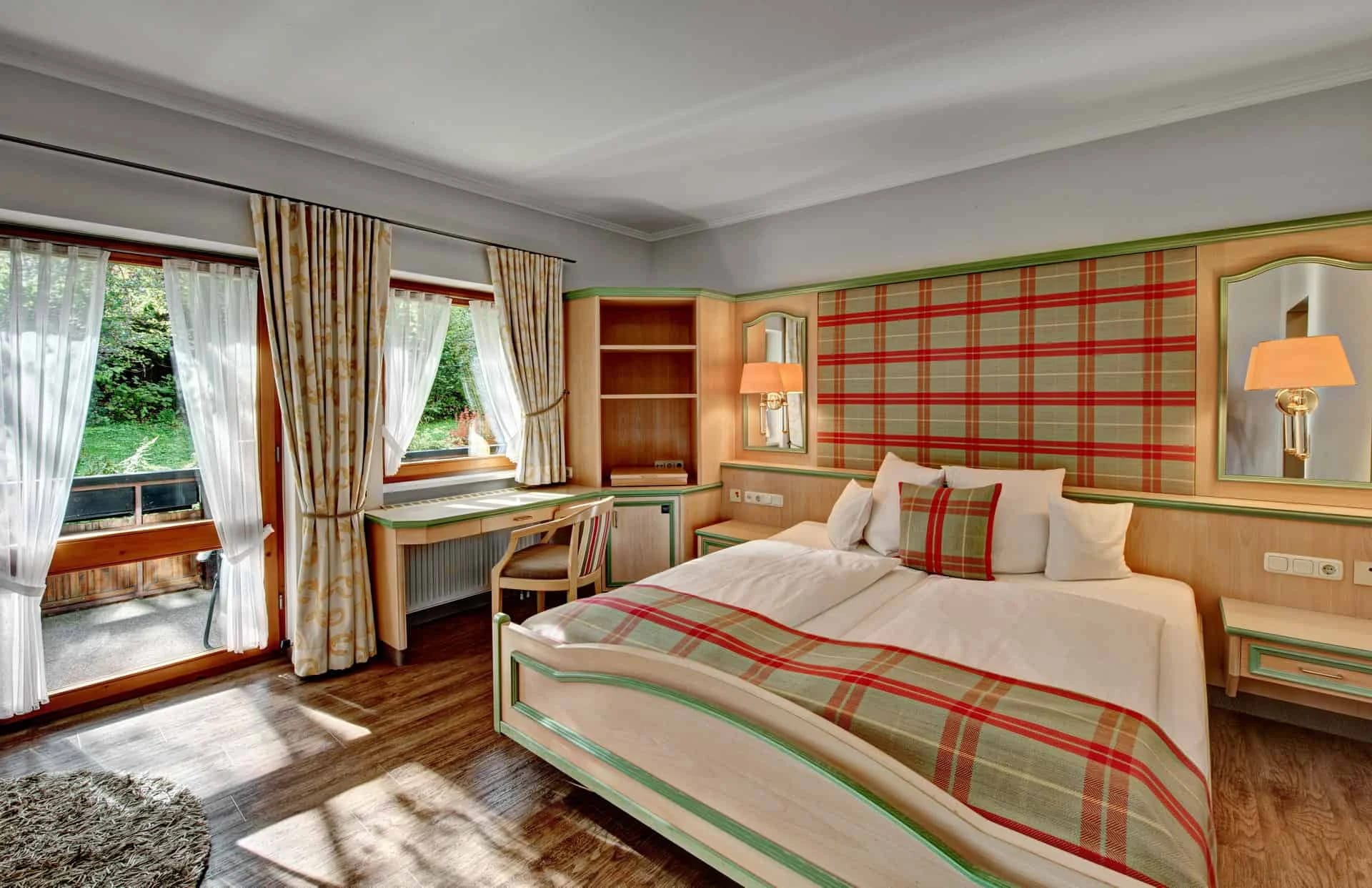 Doppelzimmer mit kariertem Kopfteil und Bettüberwurf, Schreibtisch und Balkontür