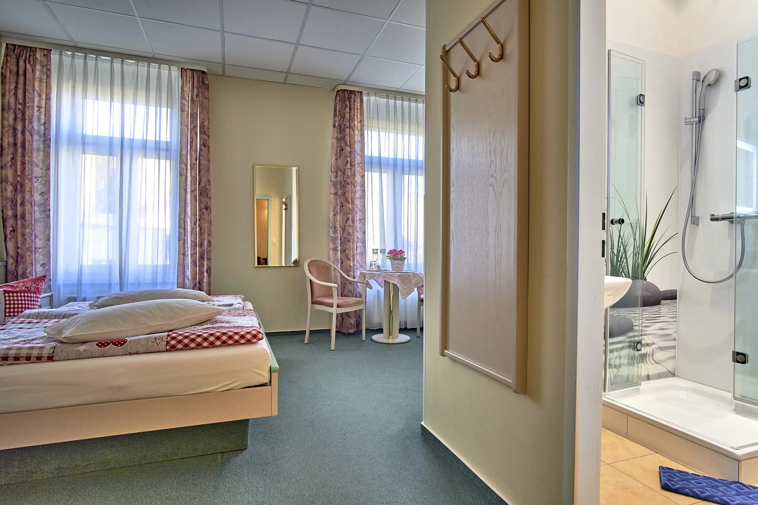 Zimmer mit Bett und offener Tür zum Bad mit gläserner Dusche