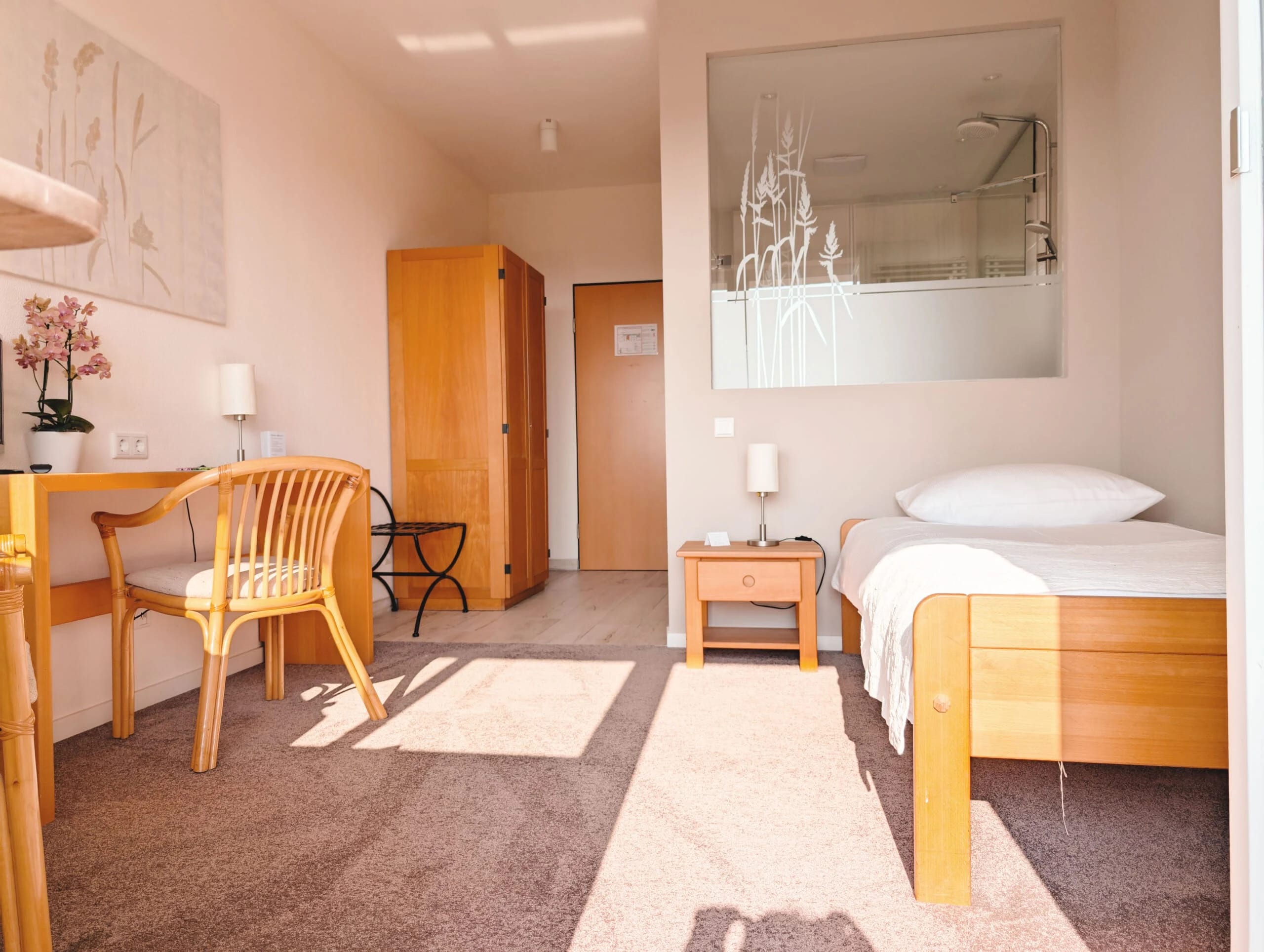 Einzelzimmer mit Bett, Schreibtisch und Sessel in warmen Tönen