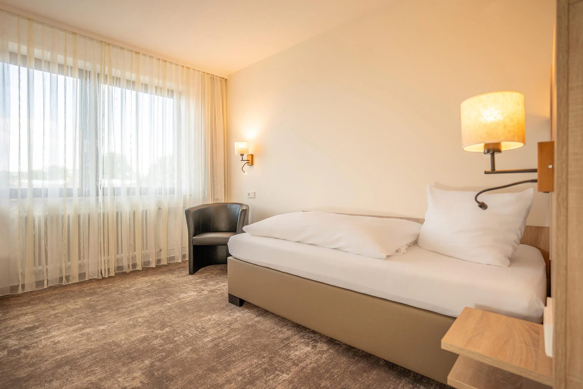 Einzelzimmer mit Bett, Sessel und Fenster