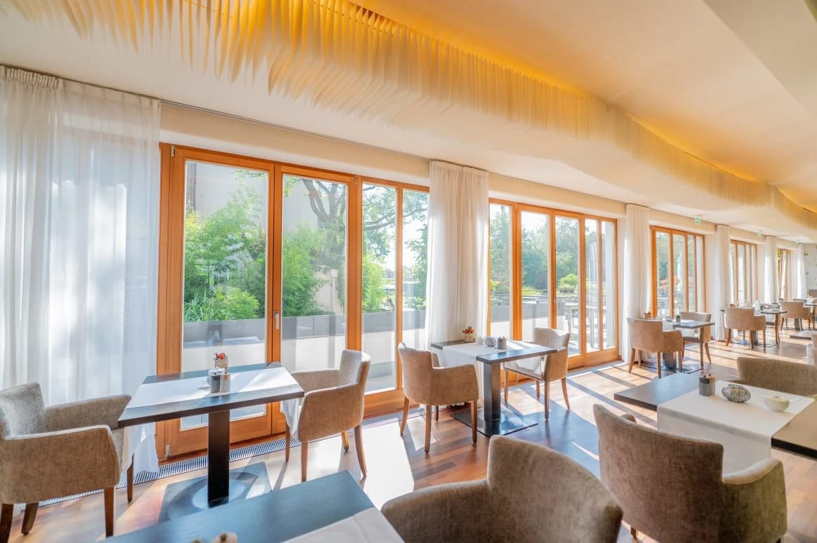 Speisesaal mit gedeckten Tischen und bodentiefen Fenstern zum Garten