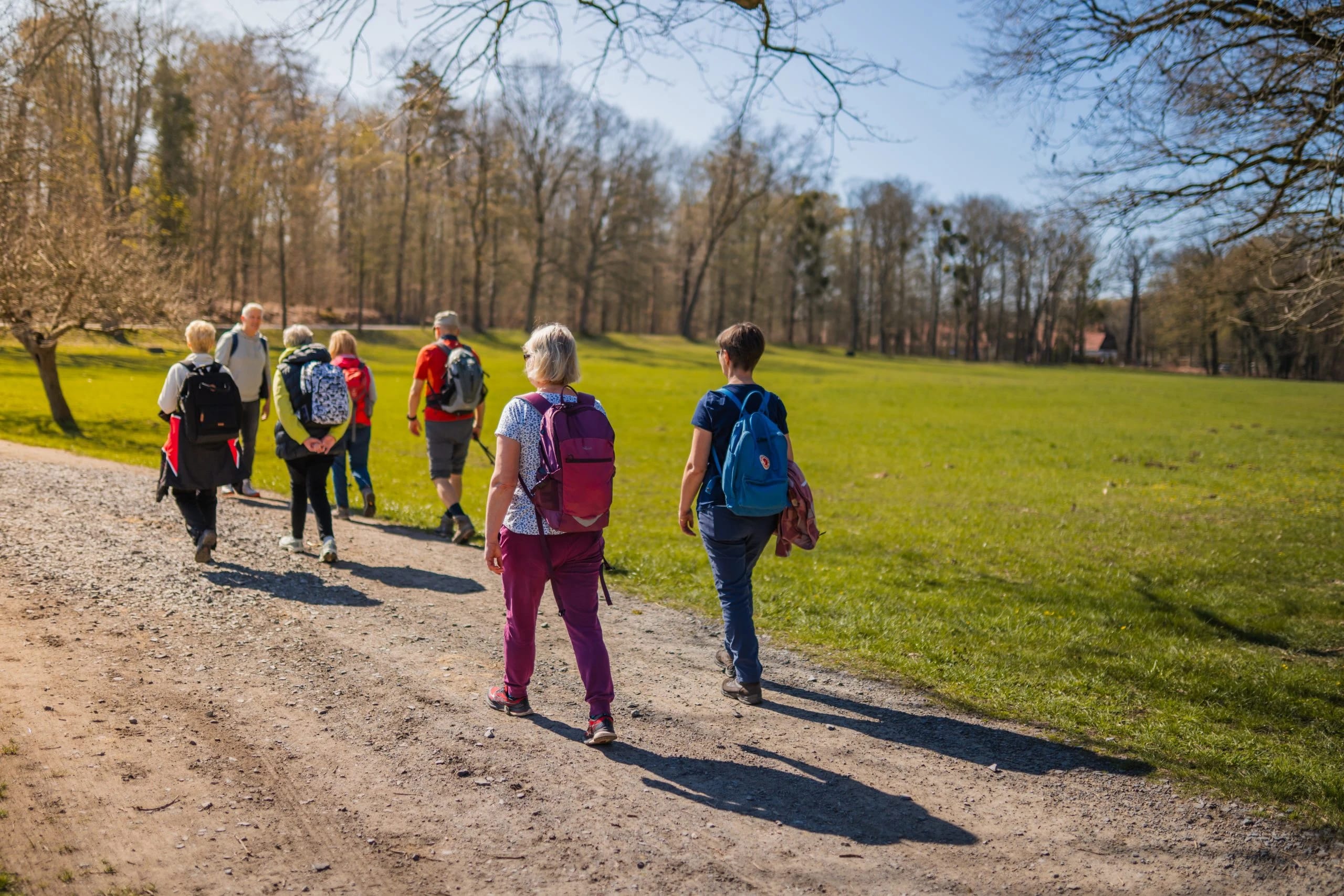 Wandergruppe mit Rucksäcken auf einer Wiese unterwegs
