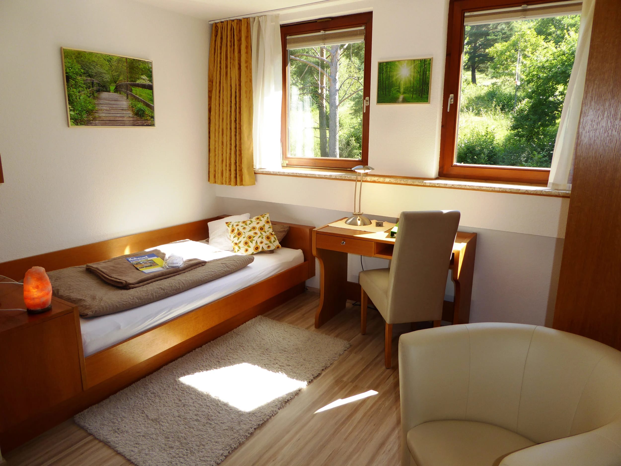 Einzelzimmer mit Bett, Schreibtisch und Fenstern mit Blick ins Grüne