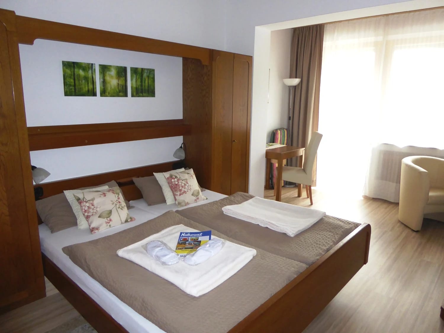 Doppelzimmer mit Holzbett, Leselampen und Sitzecke an der Balkontür