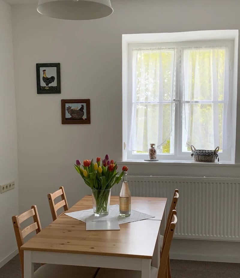 Essplatz mit Holztisch, Stühlen und Tulpenstrauß am Fenster