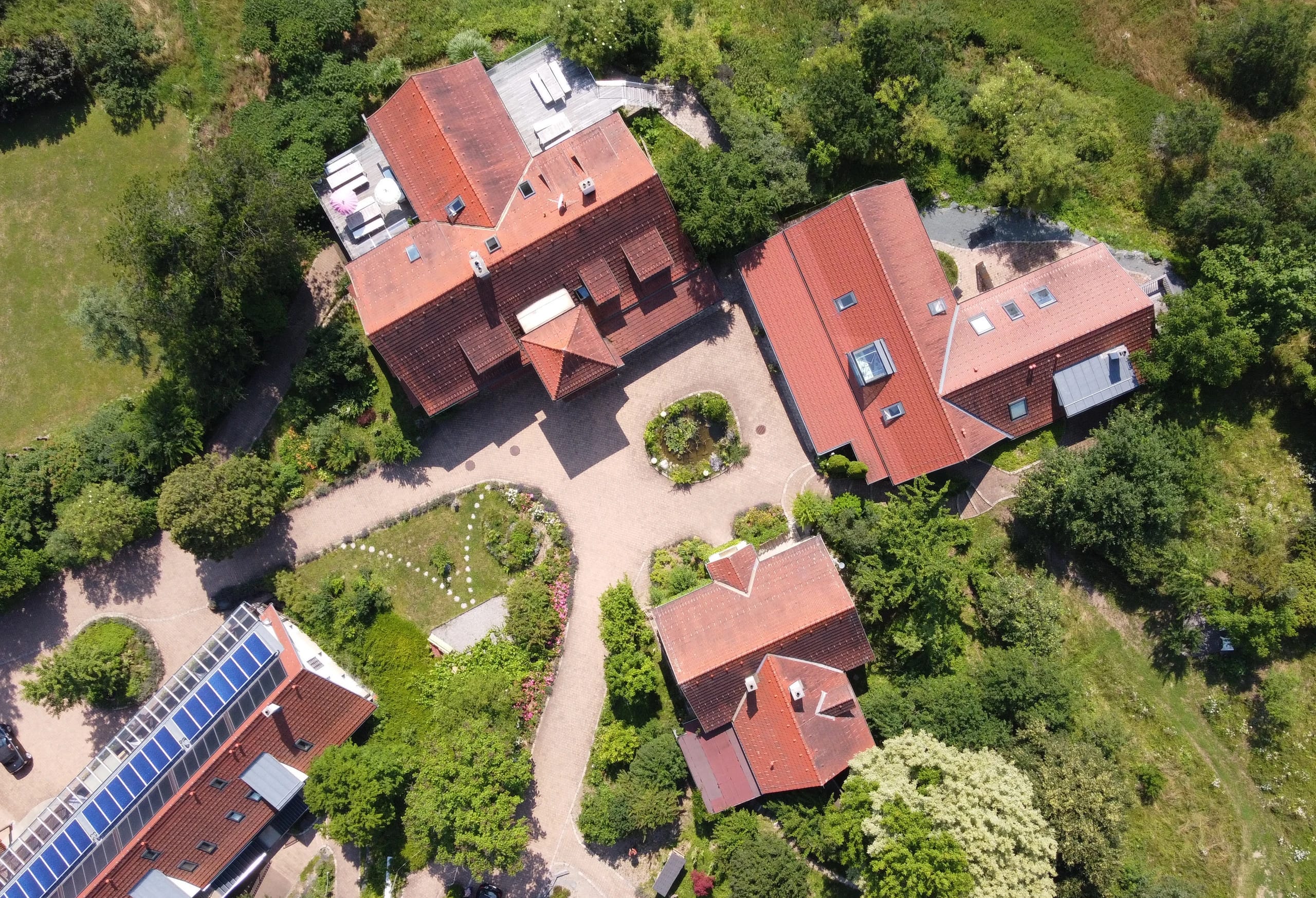 Blick von oben auf die Gebäude mit roten Dächern und den angelegten Garten
