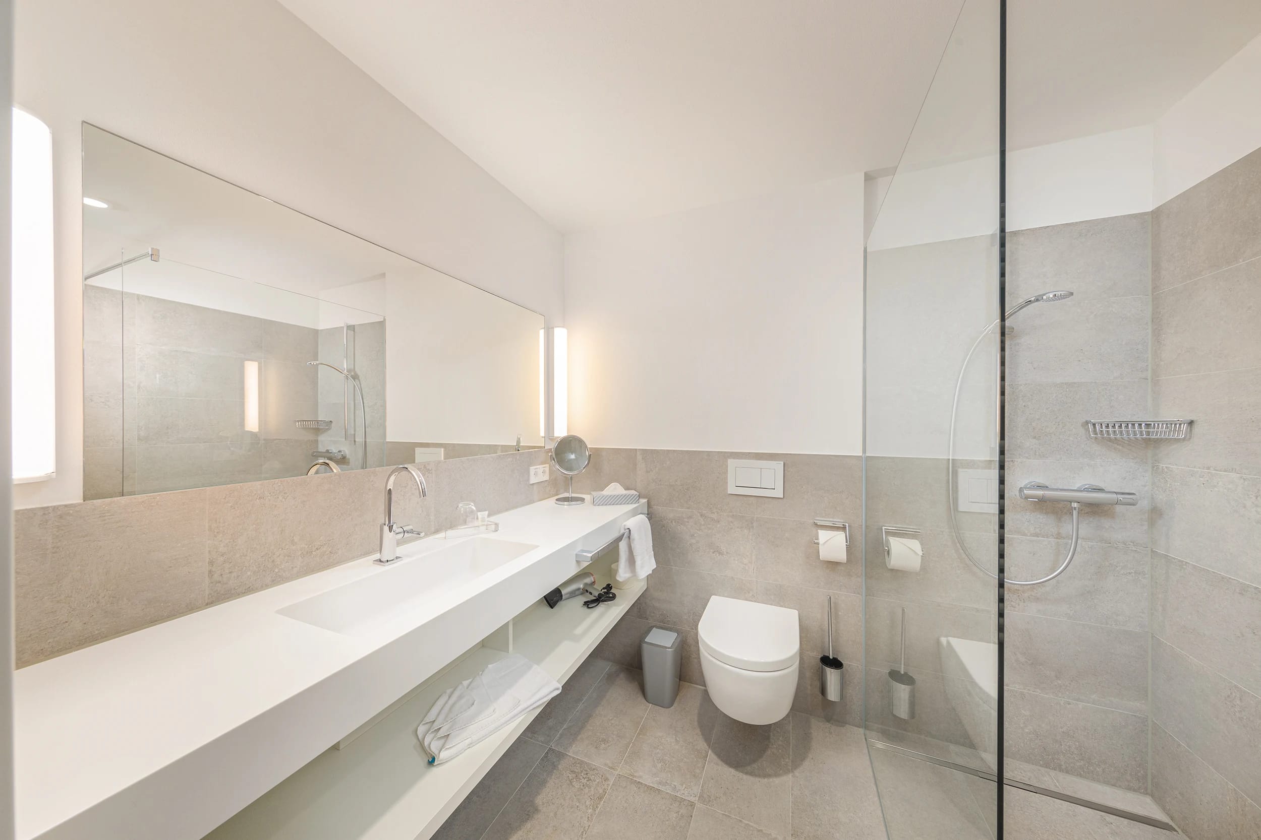 Helles Badezimmer mit langem Waschtisch, Spiegel und bodengleicher Dusche