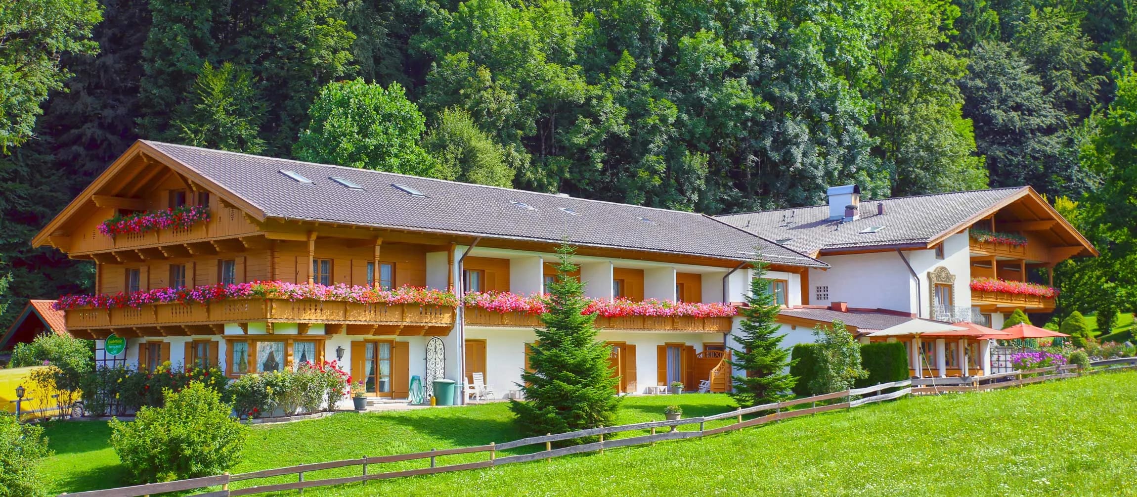 Hotelgebäude im Chalet-Stil mit Holzbalkonen und rotem Blumenschmuck, davor eine grüne Wiese