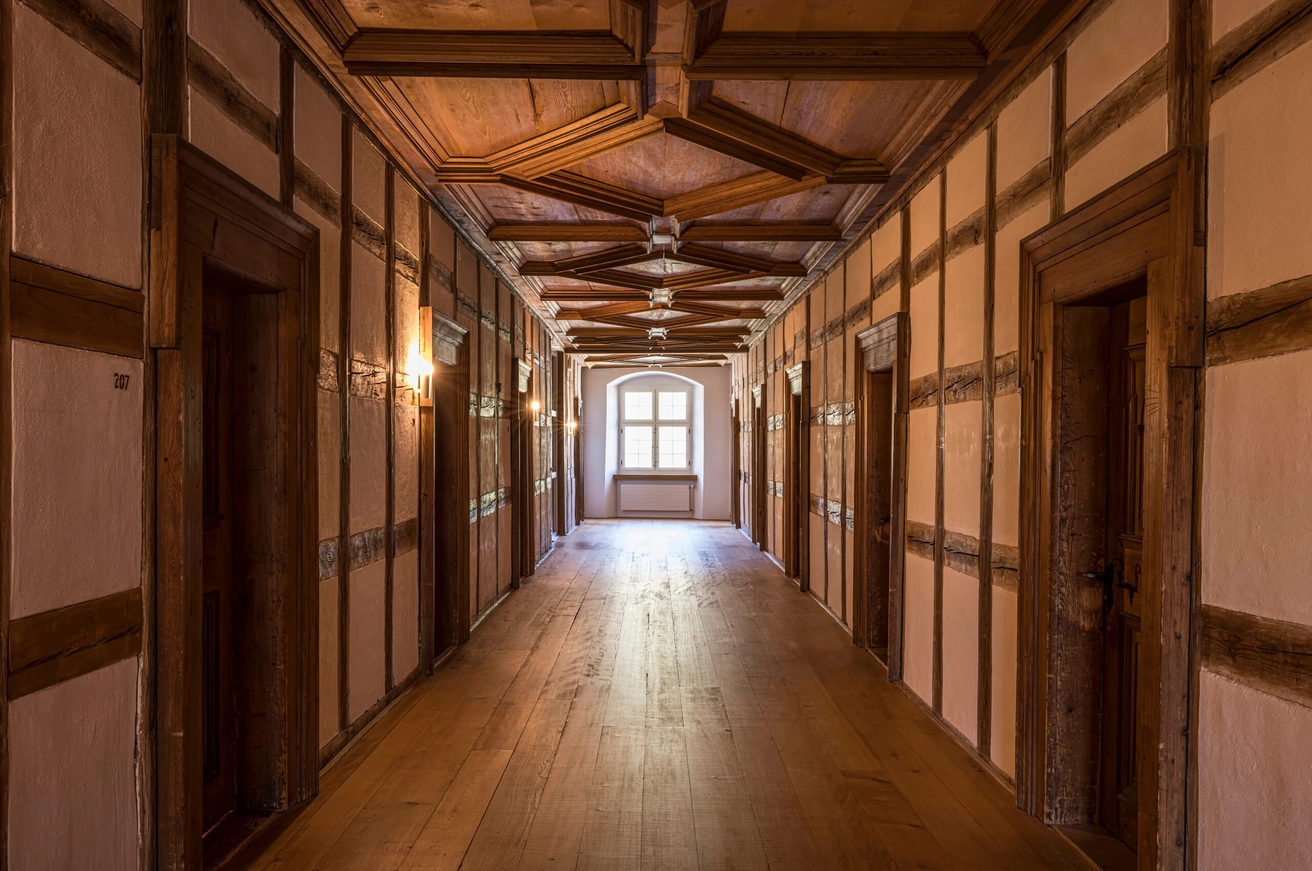 Historischer Gang mit Fachwerkwänden, hölzerner Kassettendecke und breiten Holzdielen