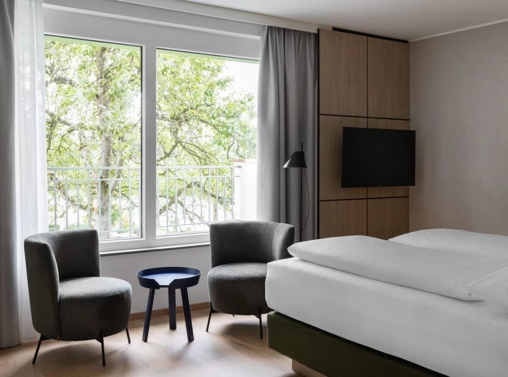 Zimmer mit zwei Polstersesseln, kleinem Beistelltisch und großem Fenster mit Blick in die Bäume