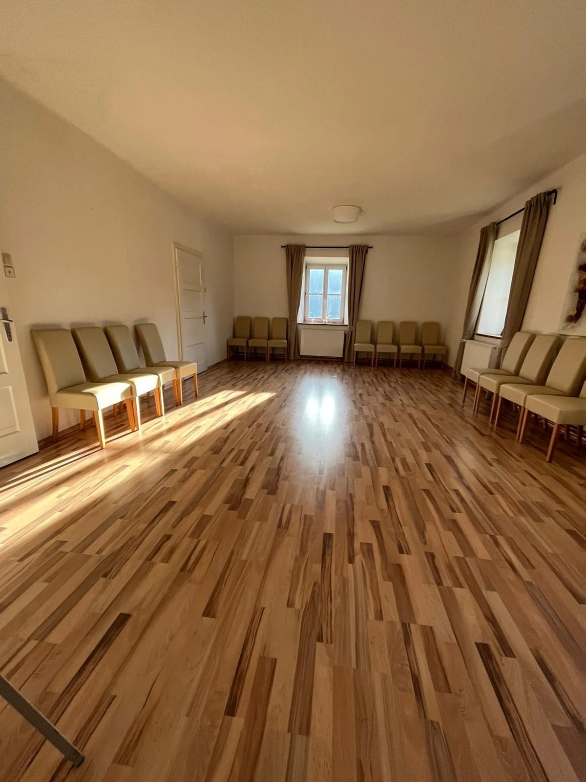Heller Raum mit Holzboden und Stuhlreihen entlang der Wände