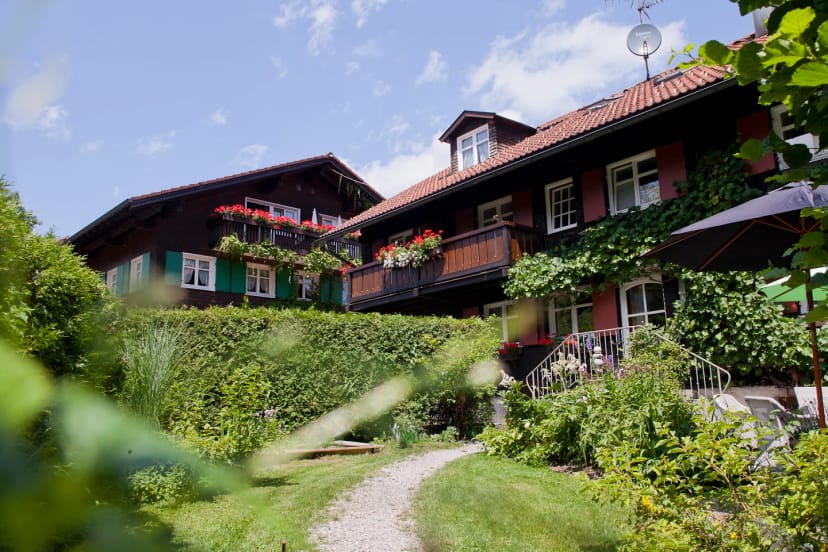 Außenansicht des Haupthauses mit dunkler Holzfassade, roten Fensterläden und Blumenbalkonen