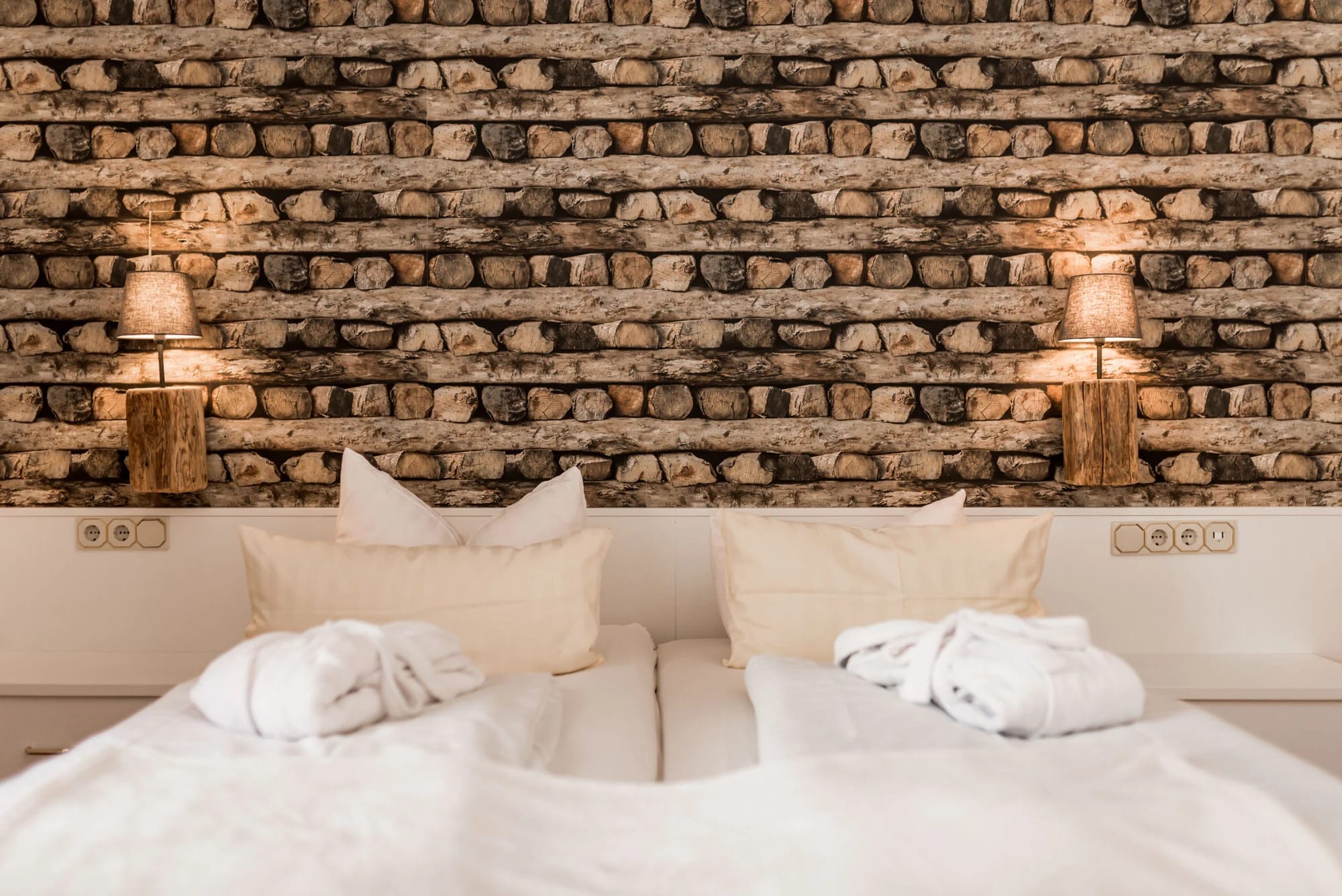 Doppelbett vor Natursteinwand mit zwei Leuchten und Bademänteln