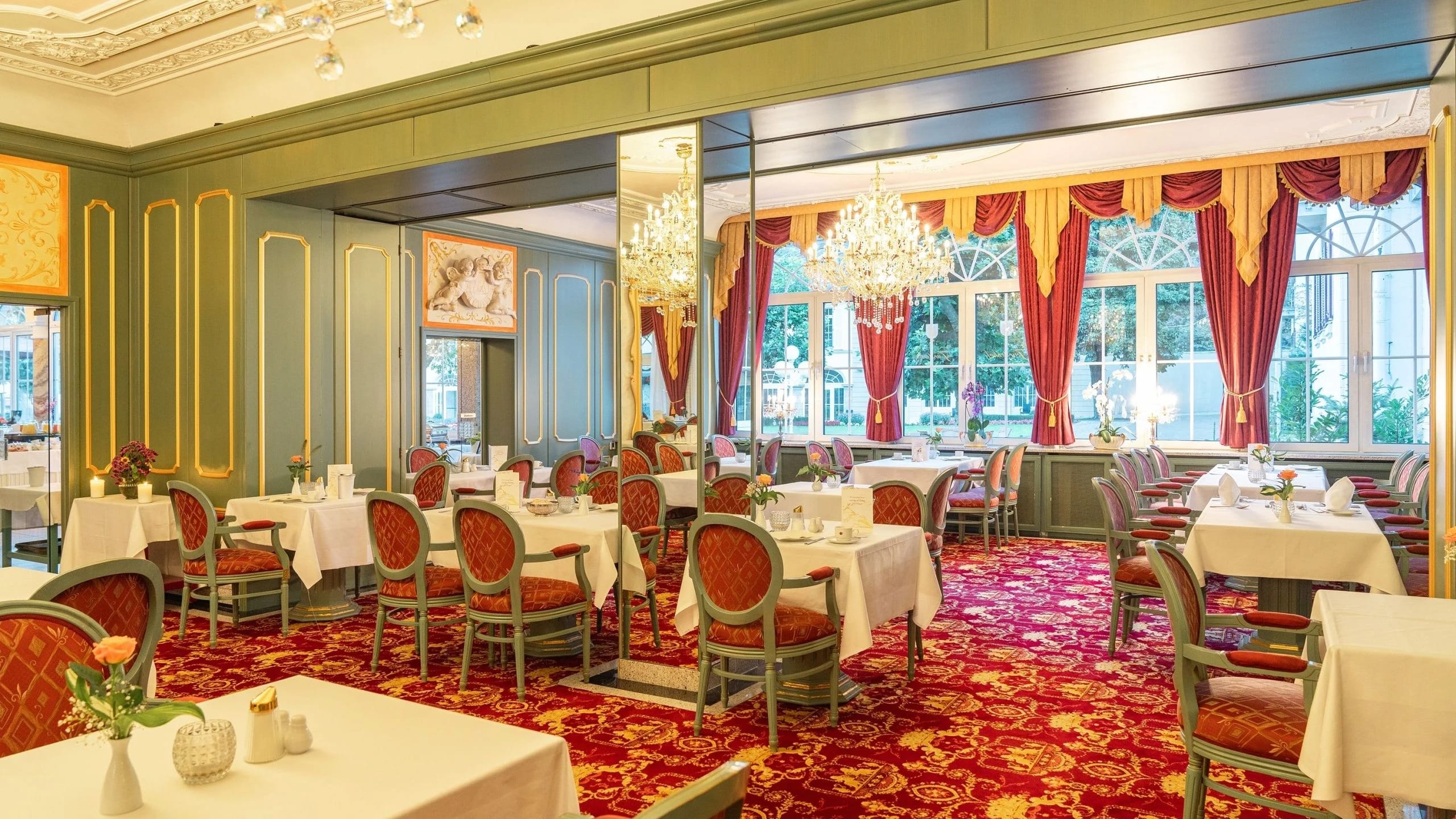 Eleganter Restaurantsaal mit rotem Teppich, Kronleuchtern und eingedeckten Tischen
