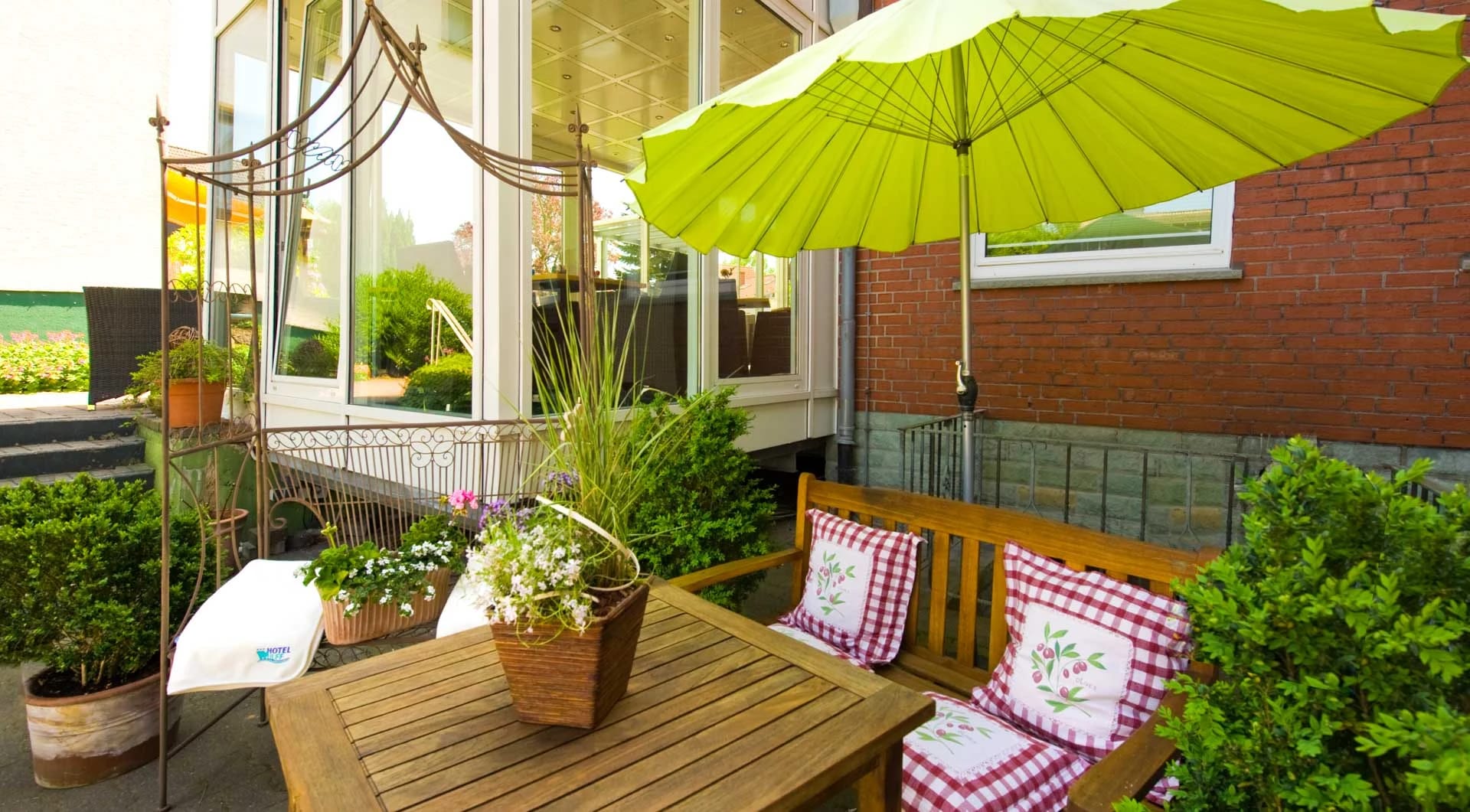 Innenhofterrasse mit Holztisch, grünem Sonnenschirm und Topfpflanzen an der Backsteinwand