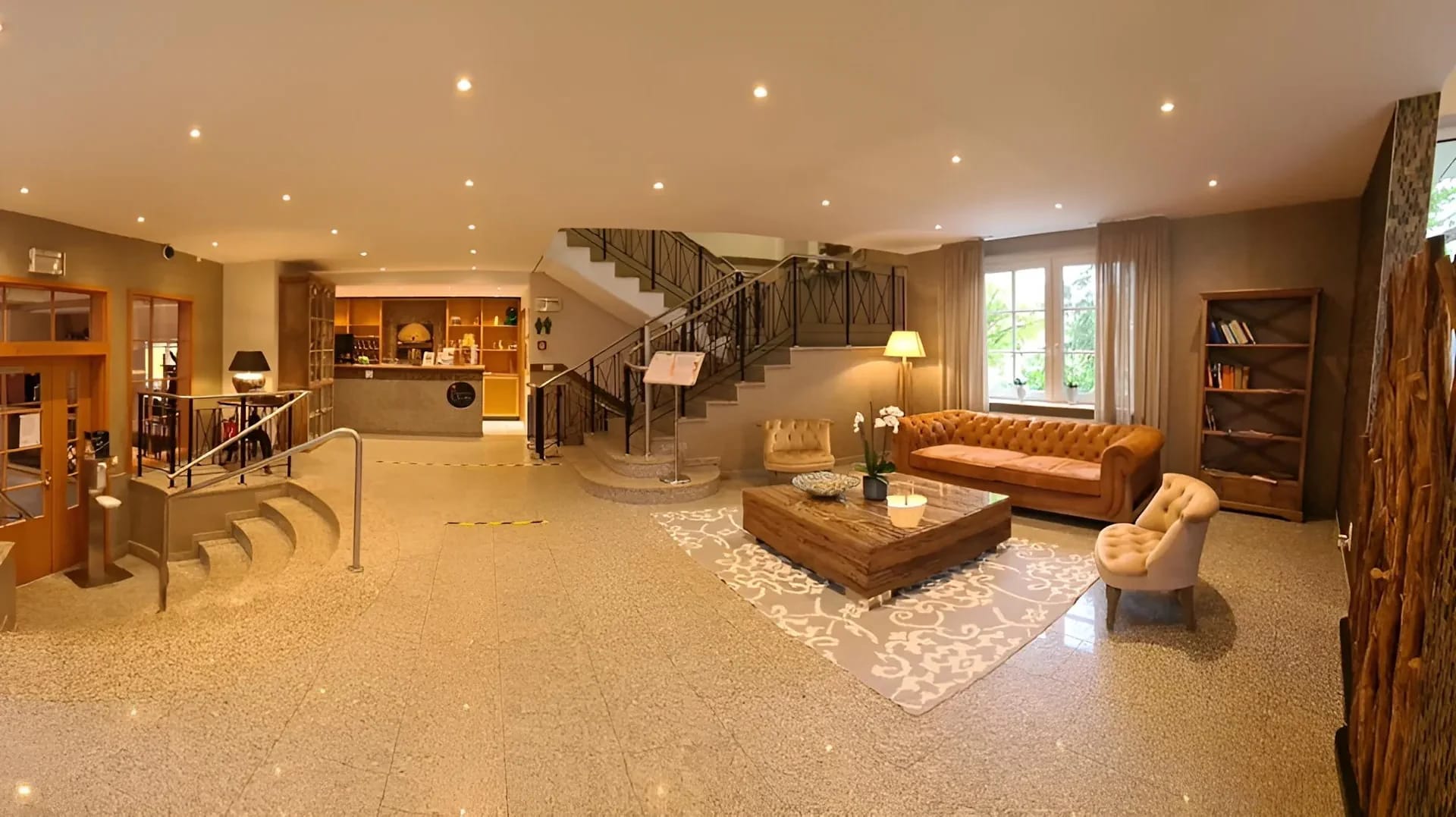 Hotellobby mit Treppenaufgang, Rezeption und Sitzbereich mit Ledersofa