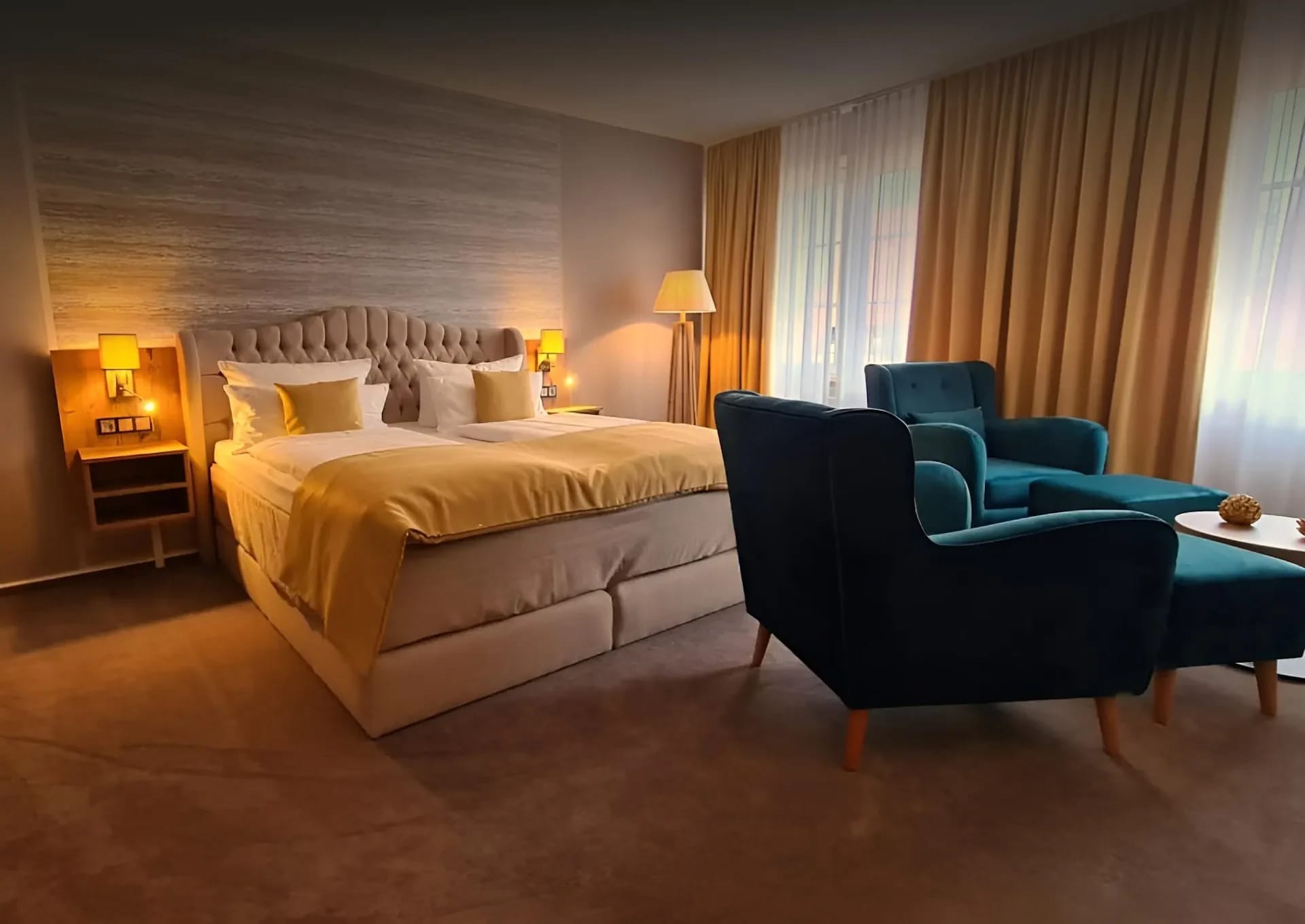 Hotelzimmer mit Doppelbett, zwei petrolfarbenen Sesseln und Fenster mit Vorhängen