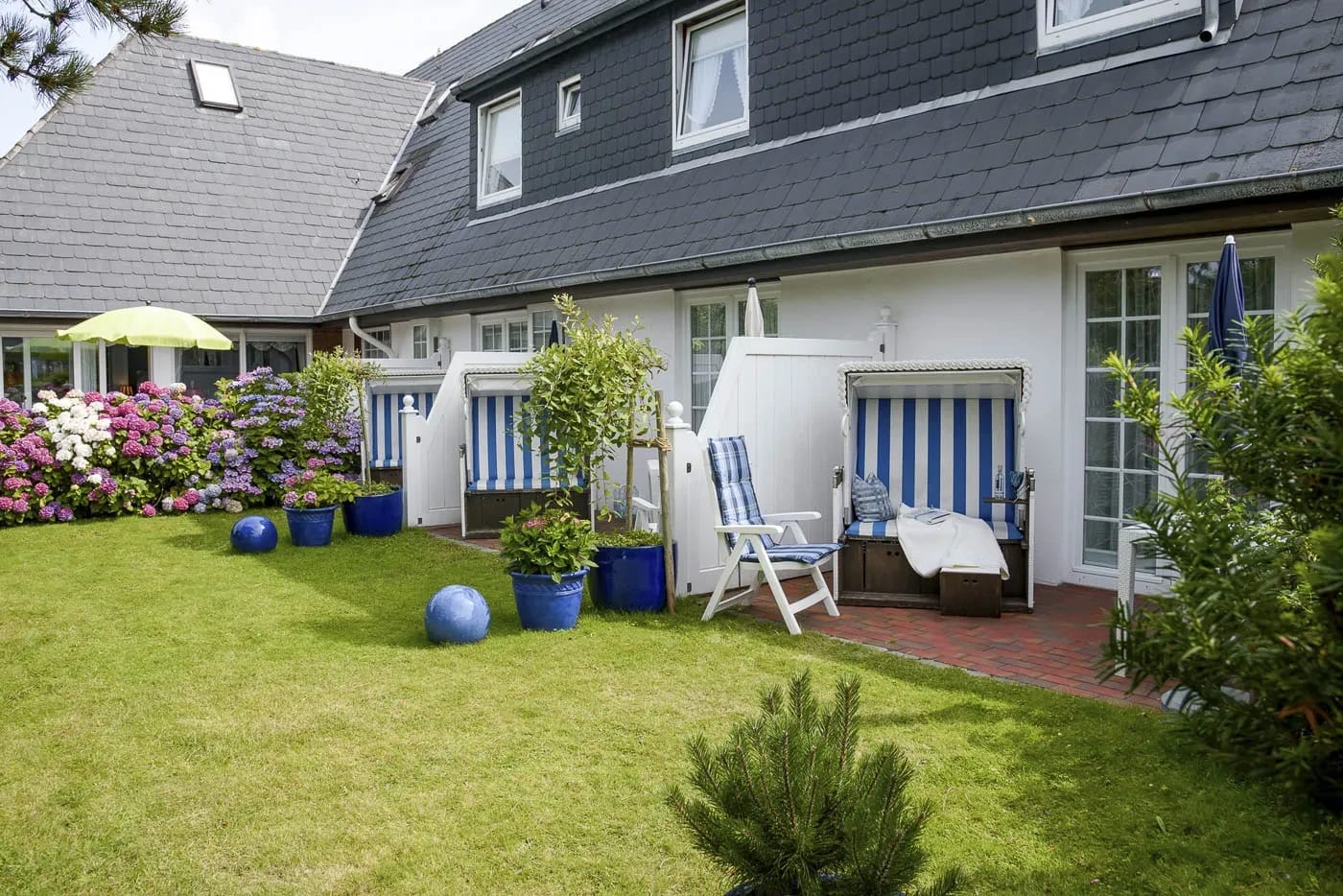 Rückseite des Hotels mit Gartenterrasse, Rasenfläche und blau-weißen Strandkörben