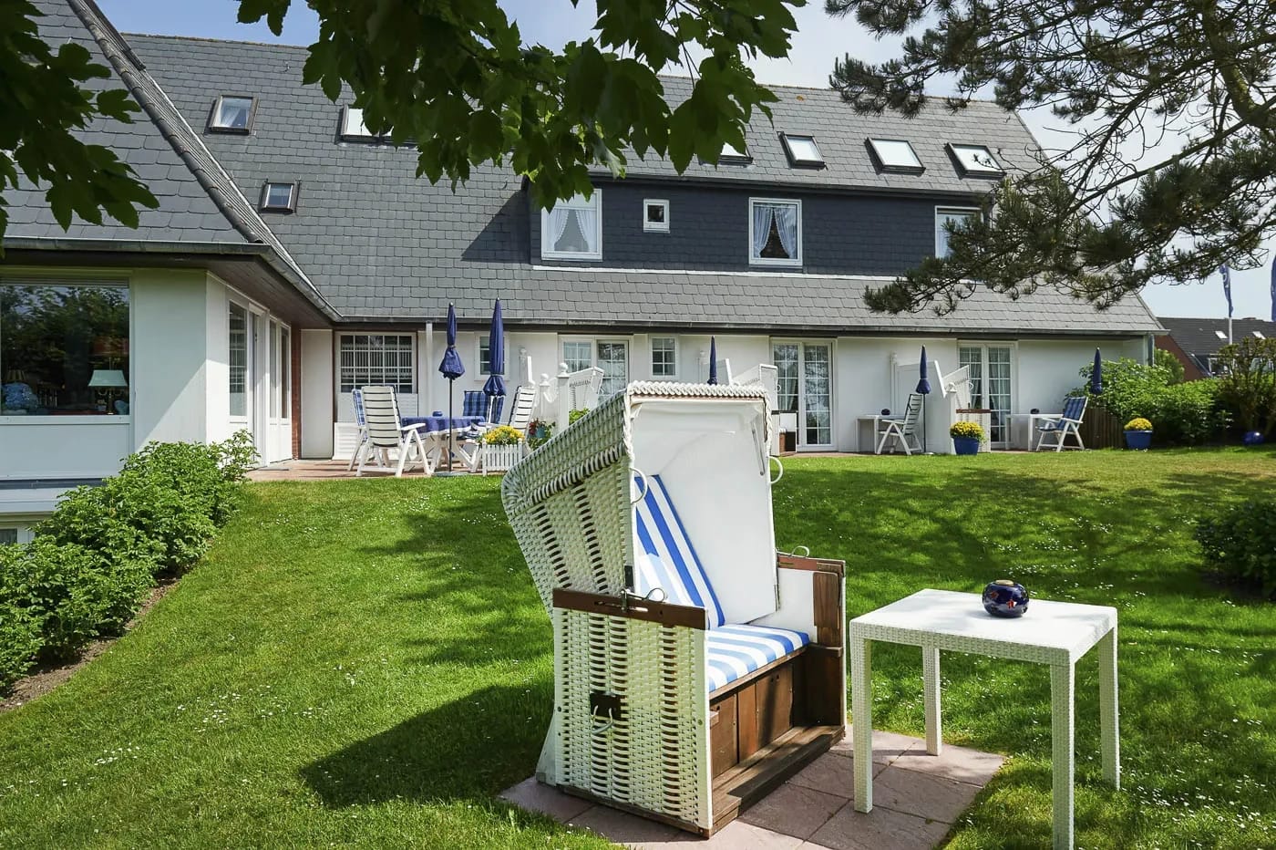 Hausrückseite mit Dachgauben, Terrasse und weißem Strandkorb im Garten