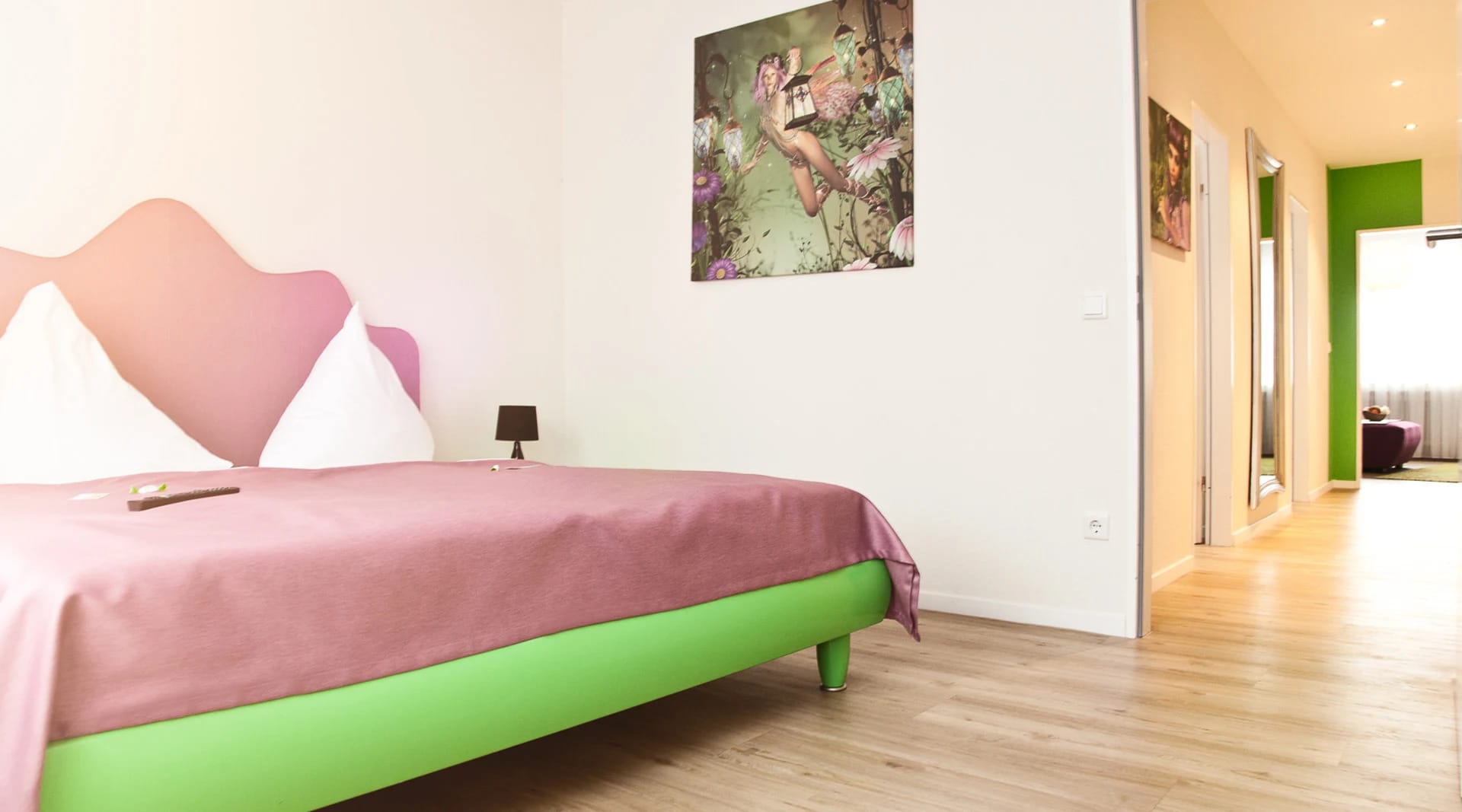 Zimmer mit grünem Bettgestell, rosa Tagesdecke und großformatigem Blumenbild