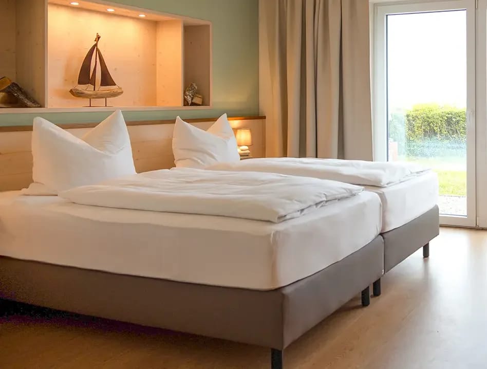 Zweibettzimmer mit zwei Boxspringbetten, Holzwand mit Deko-Segelschiff und Fenster zum Garten