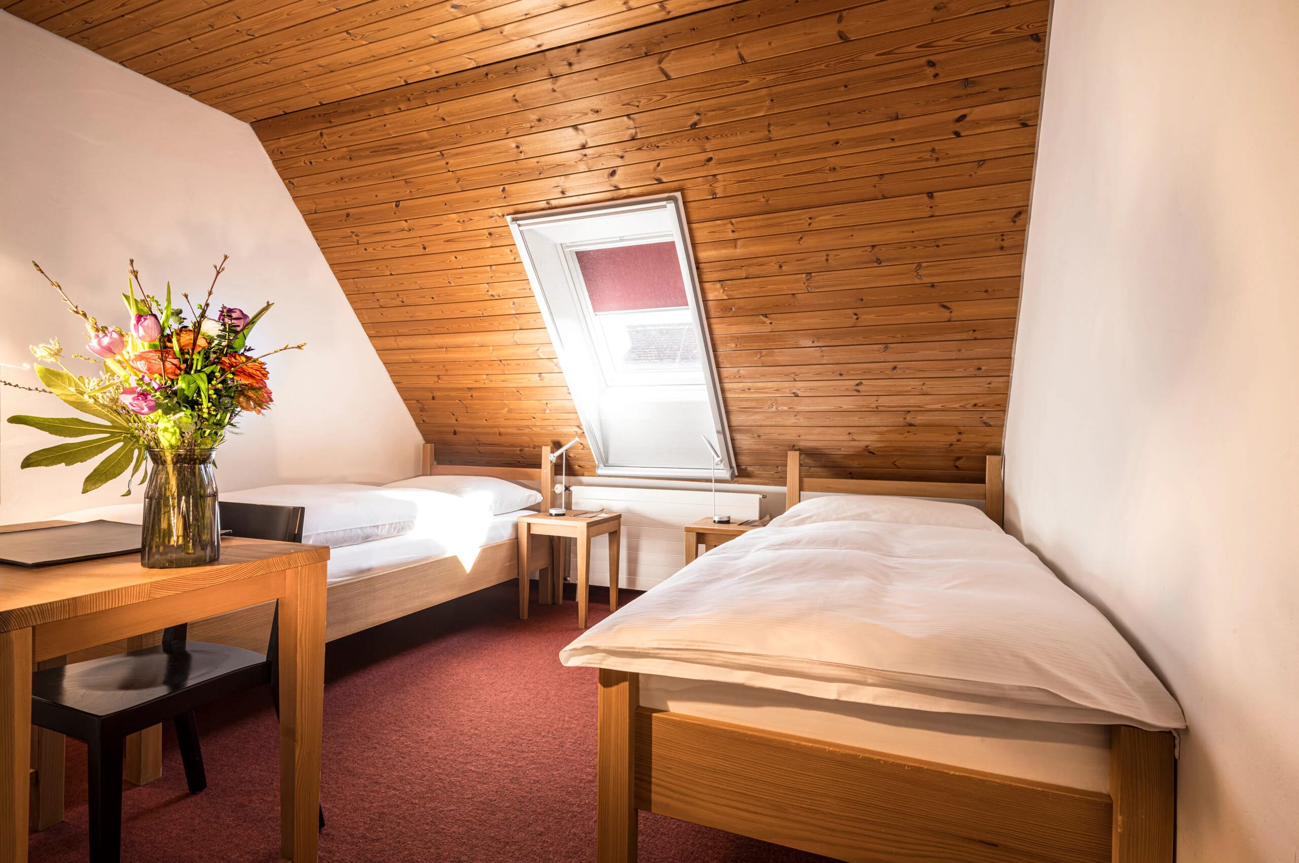 Dachzimmer mit Holzverkleidung, Dachfenster, zwei Einzelbetten und rotem Teppich