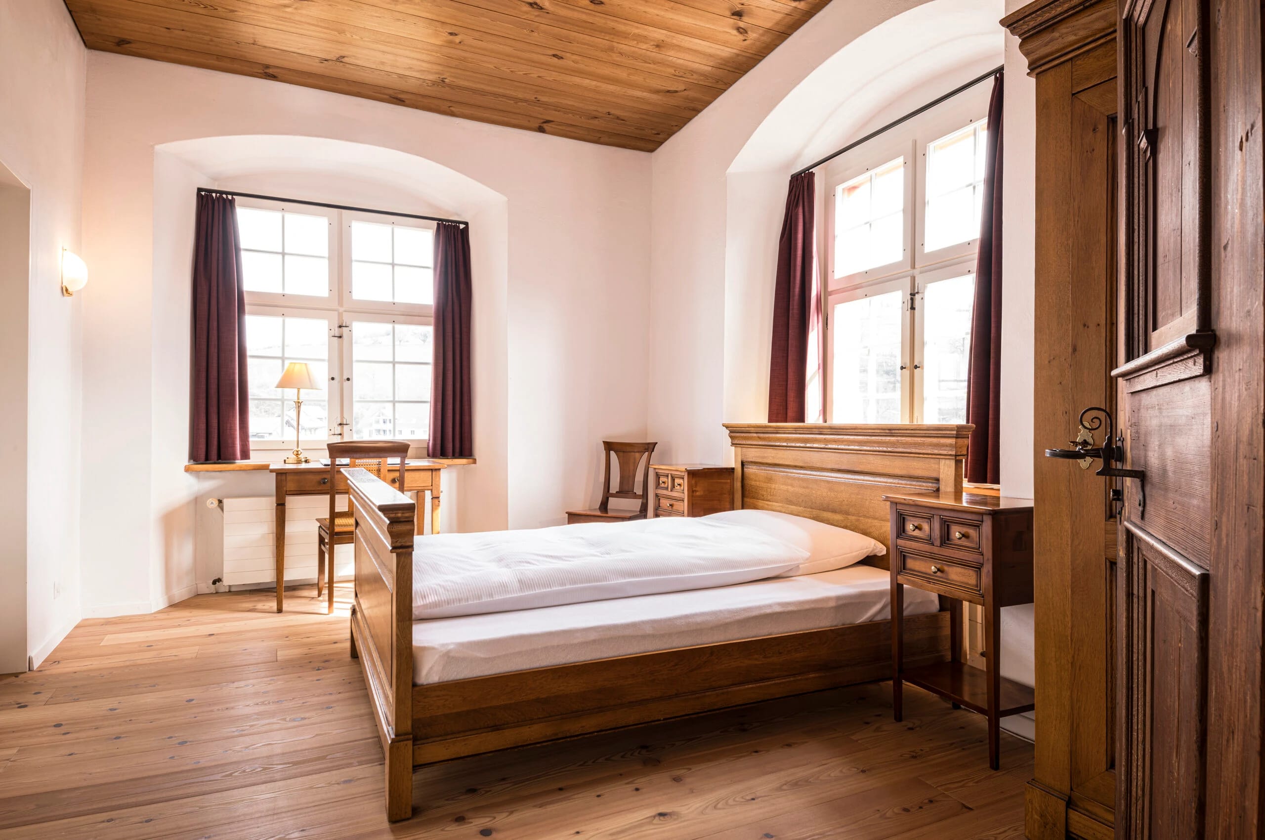 Hotelzimmer mit Holzdecke, Dielenboden, Holzbett und zwei Rundbogenfenstern
