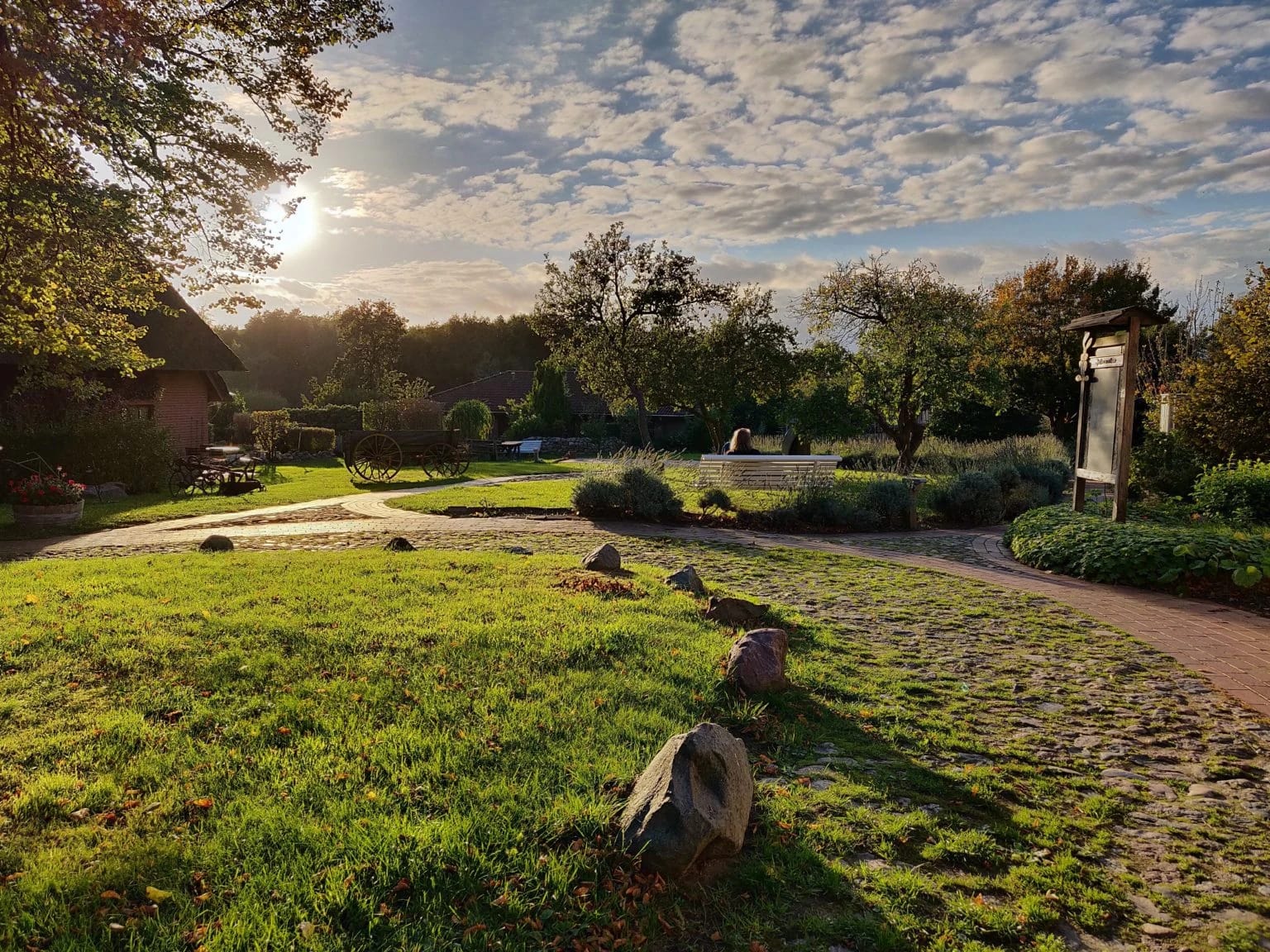 Gartenanlage mit Rasenfläche, Findlingen und geschwungenem Weg im Abendlicht