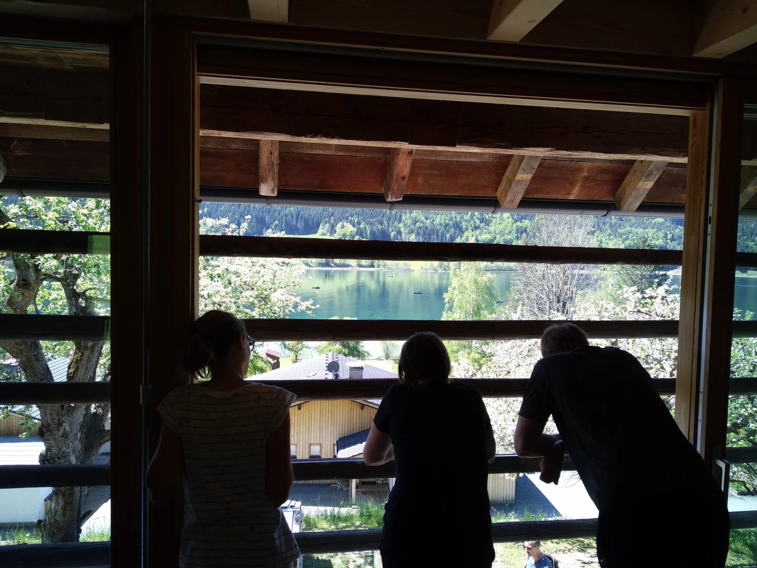 Personen blicken durch ein großes Fenster auf den Weissensee