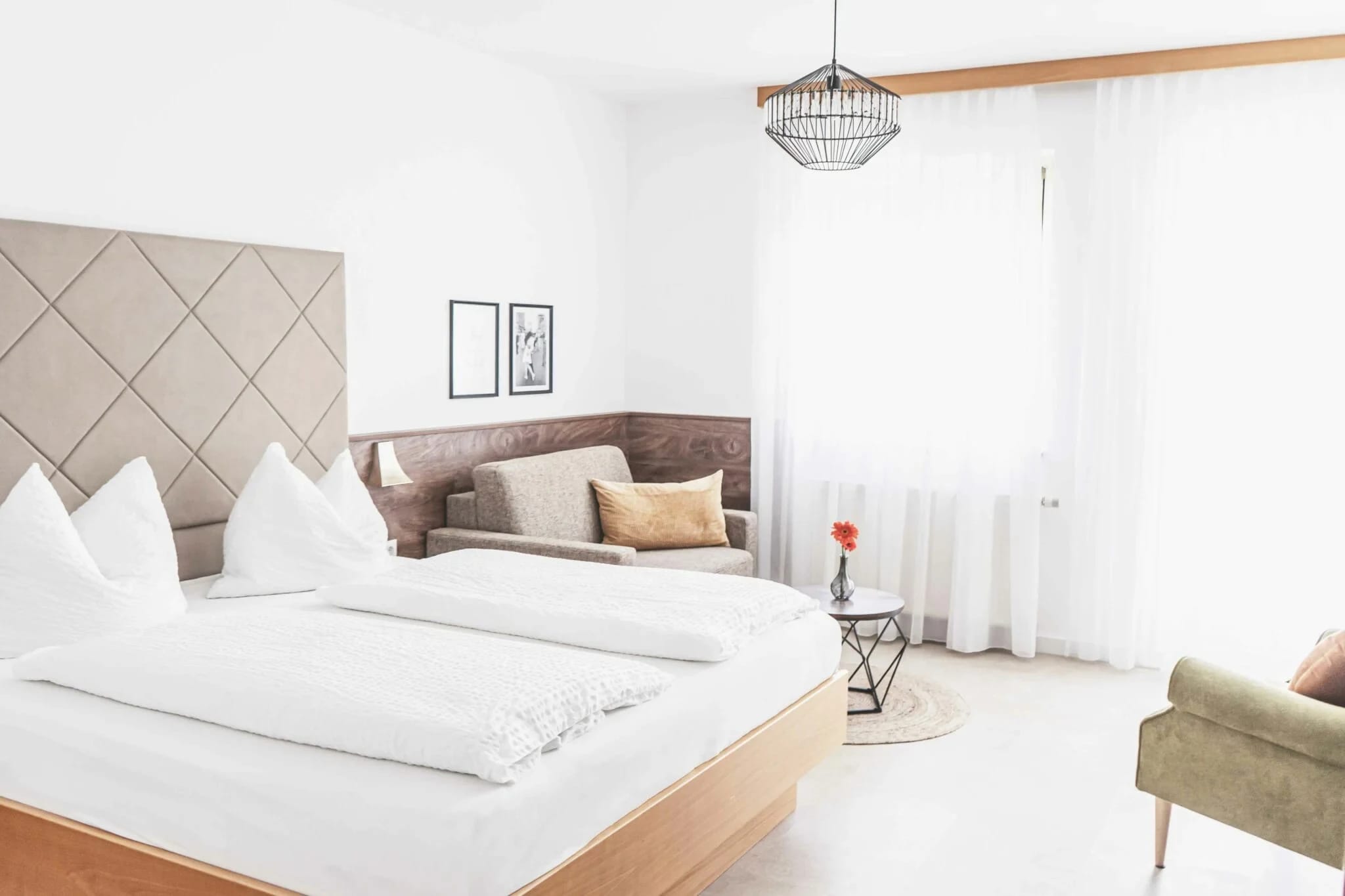Helles Zimmer mit weißem Doppelbett, Vorhängen und Sitzecke
