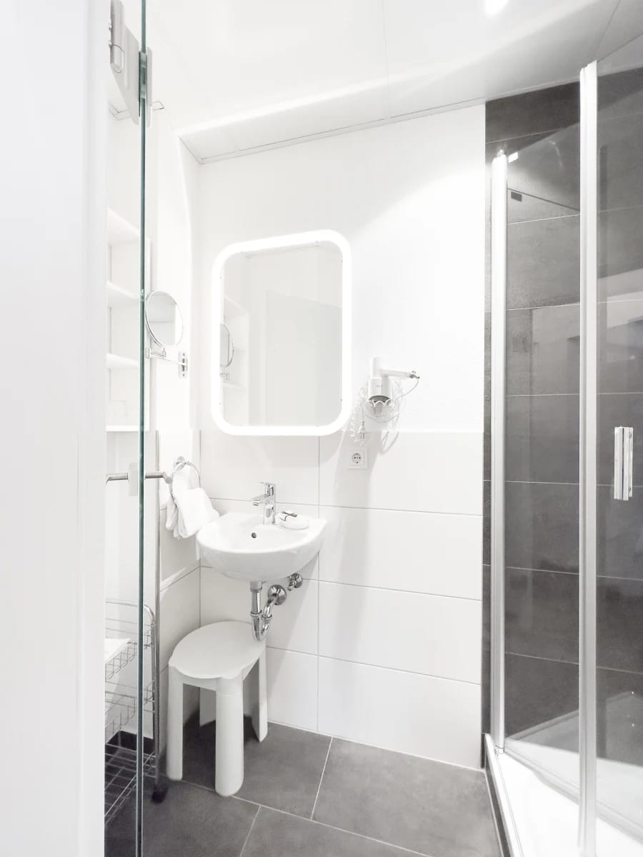 Badezimmer mit Waschbecken, beleuchtetem Spiegel und Dusche