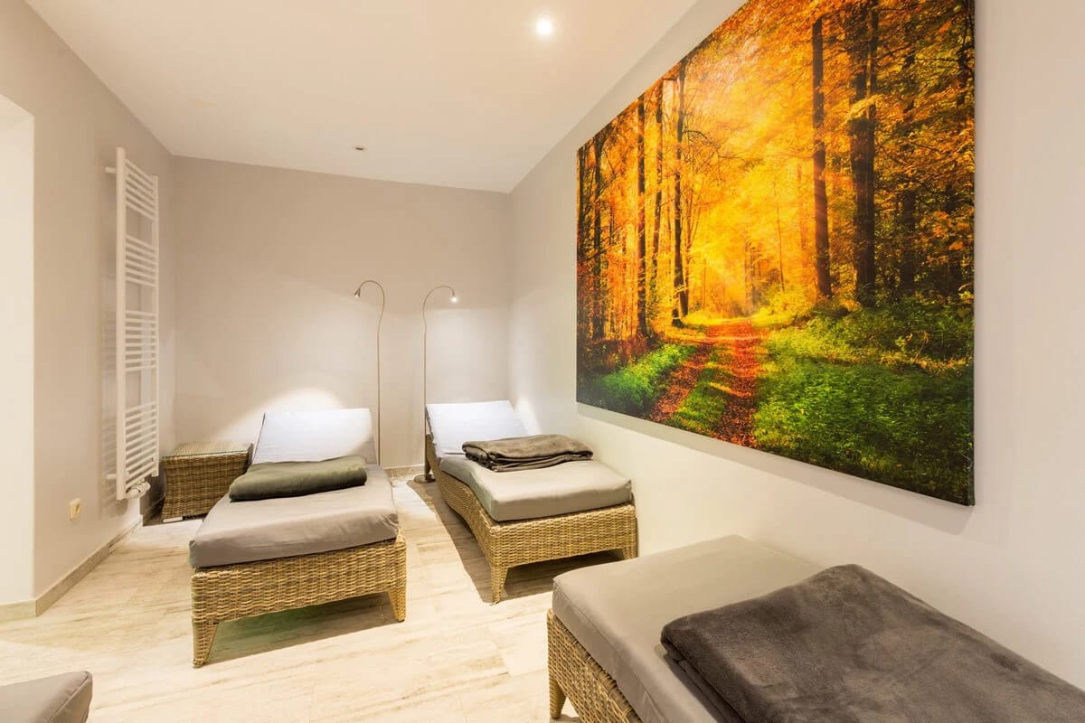Ruheraum mit drei Liegen, Handtüchern und großem Waldmotiv an der Wand