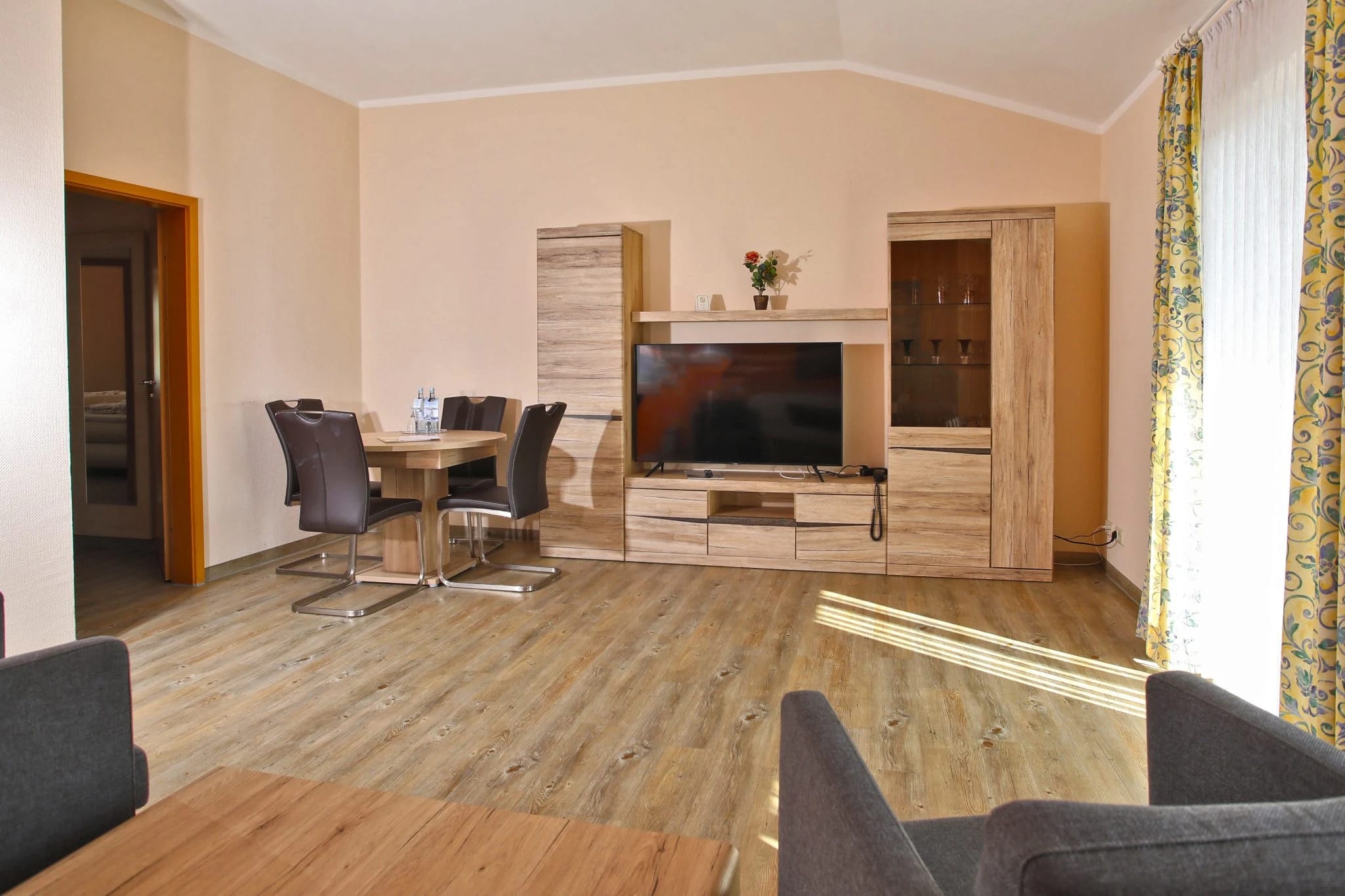 Wohnraum mit Esstisch, dunklen Stühlen, Sofa und Sideboard mit Fernseher auf Holzboden