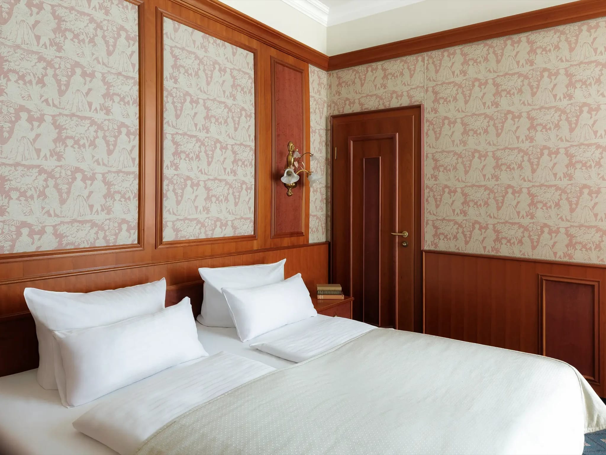 Zimmer mit Doppelbett, gemusterter Wandtapete und dunkler Holzvertäfelung