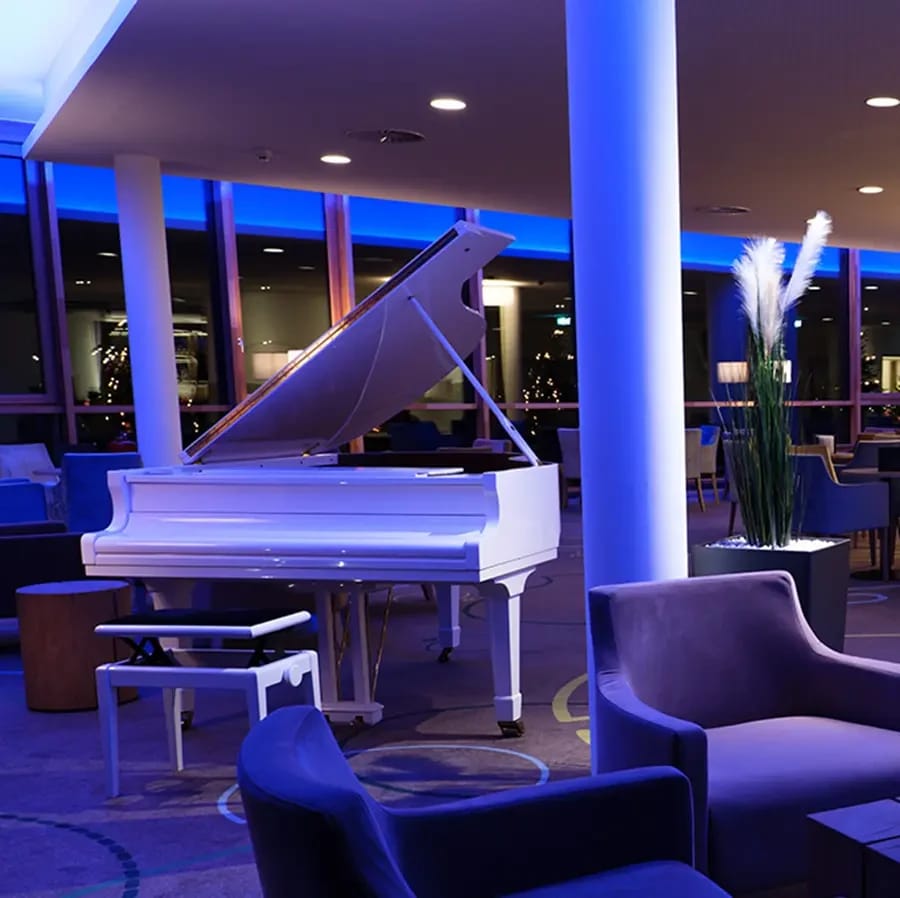 Bar-Lounge mit weißem Flügel, Sesseln und blauer Abendbeleuchtung
