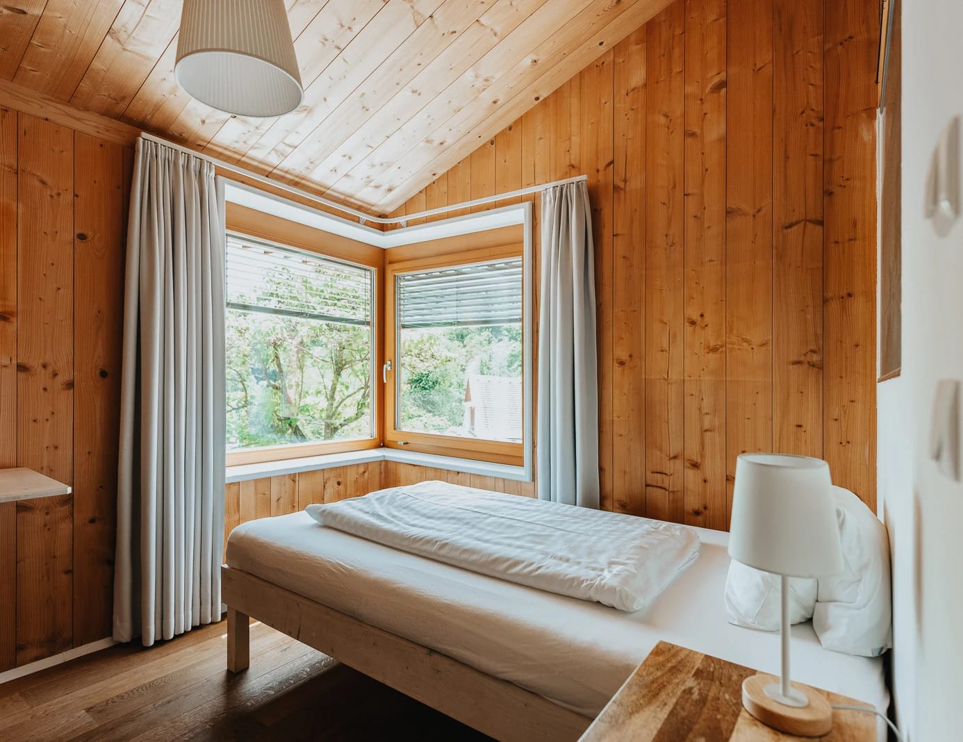 Schlafzimmer mit Holzverkleidung an Wänden und Decke und Fenster ins Grüne
