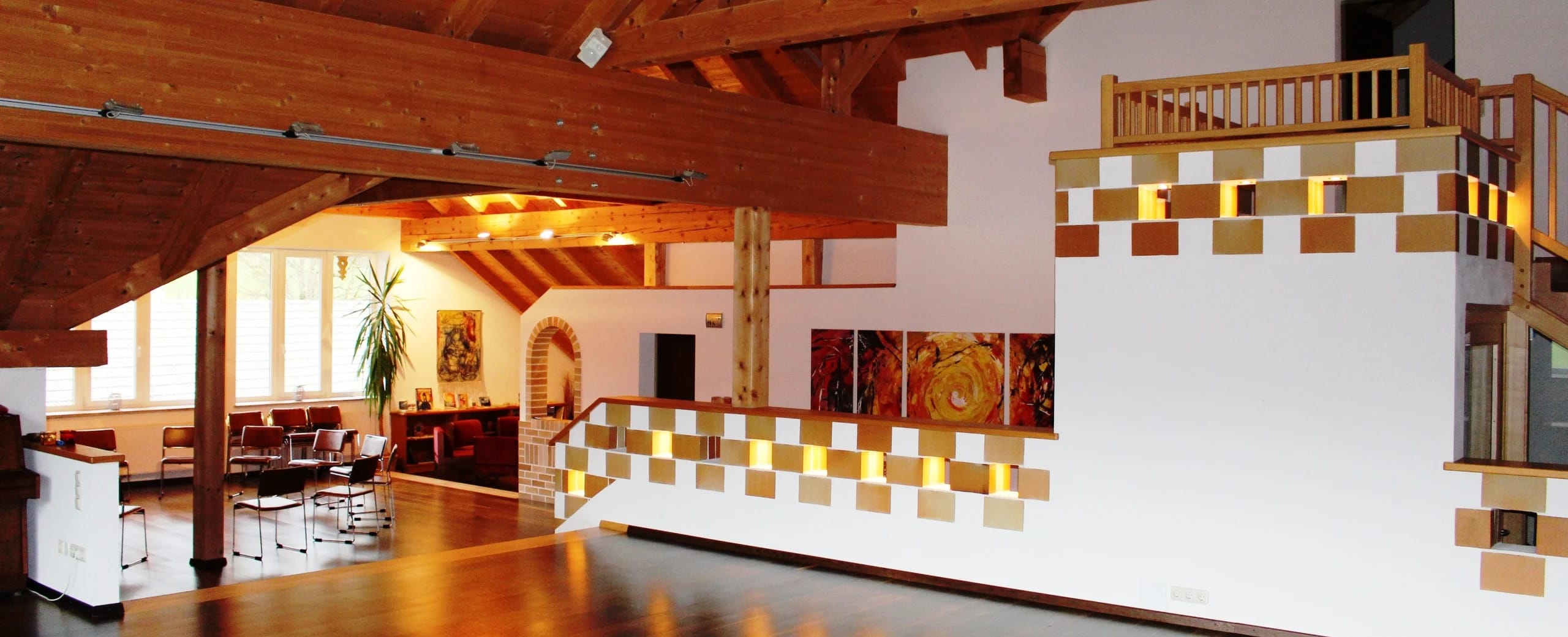 Seminarraum im Klosterhof mit offenem Holzdachstuhl, Sitzgruppe und goldener Mosaikwand